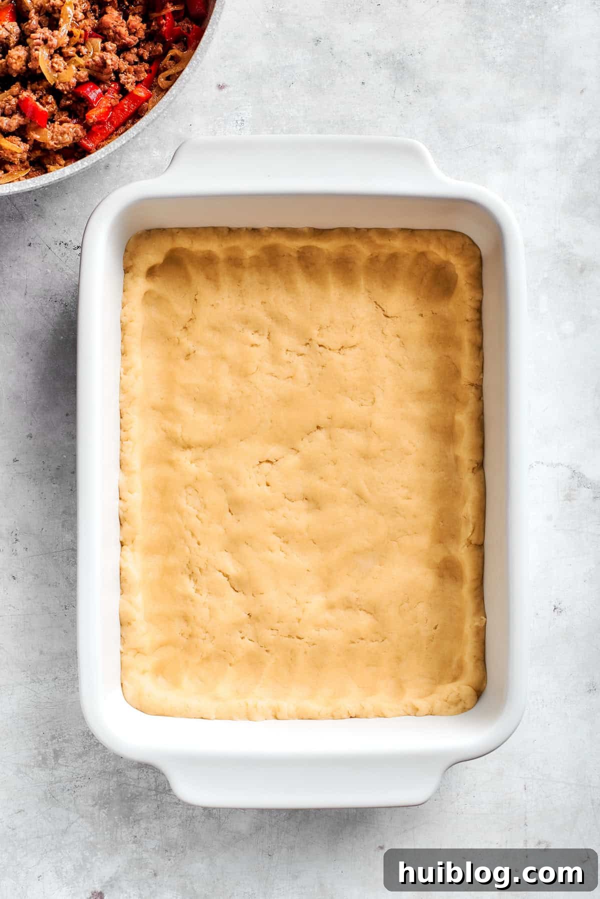 Pressing the biscuit dough evenly into the bottom of a baking dish.