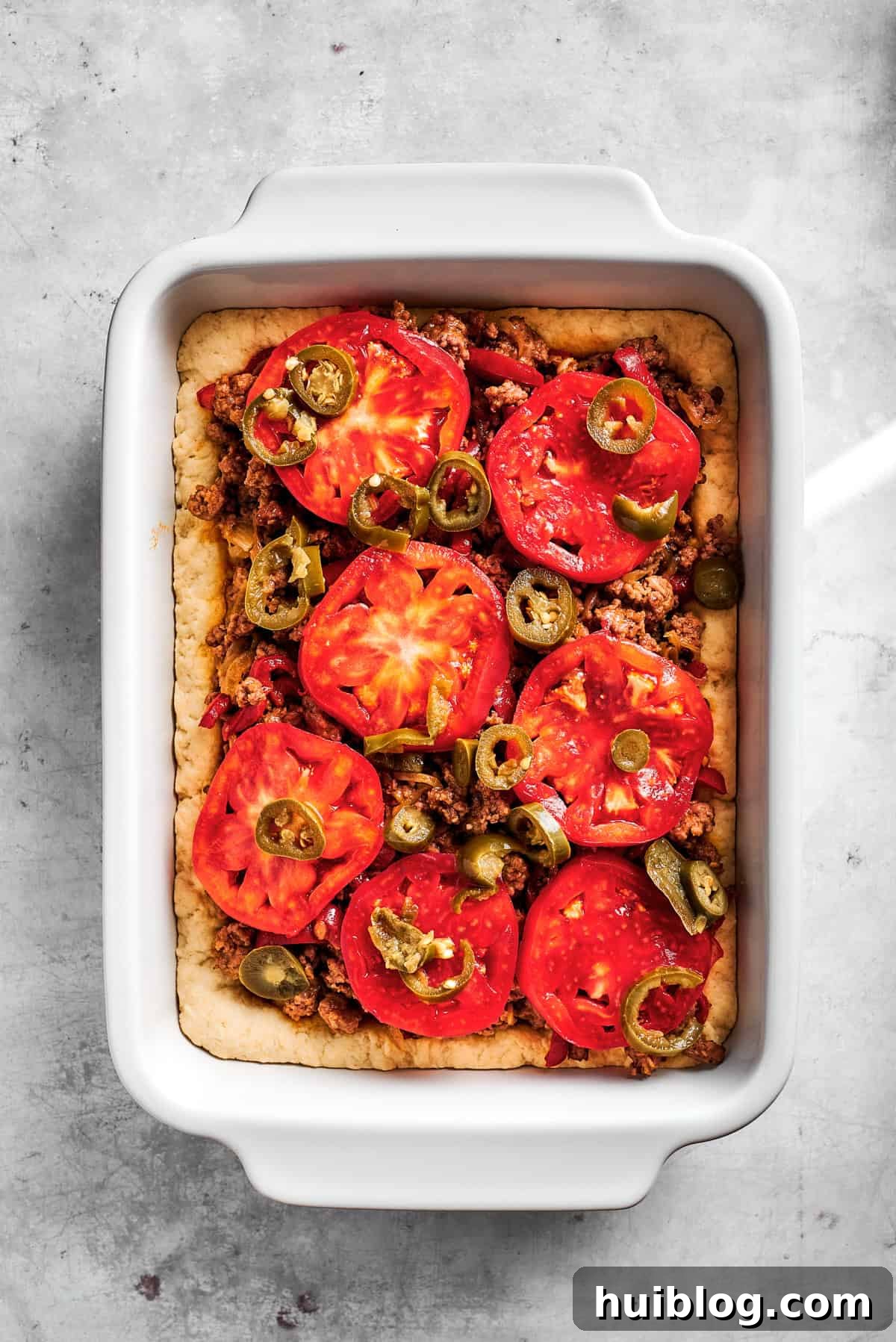 Layering fresh tomato slices over the meat and biscuit base.