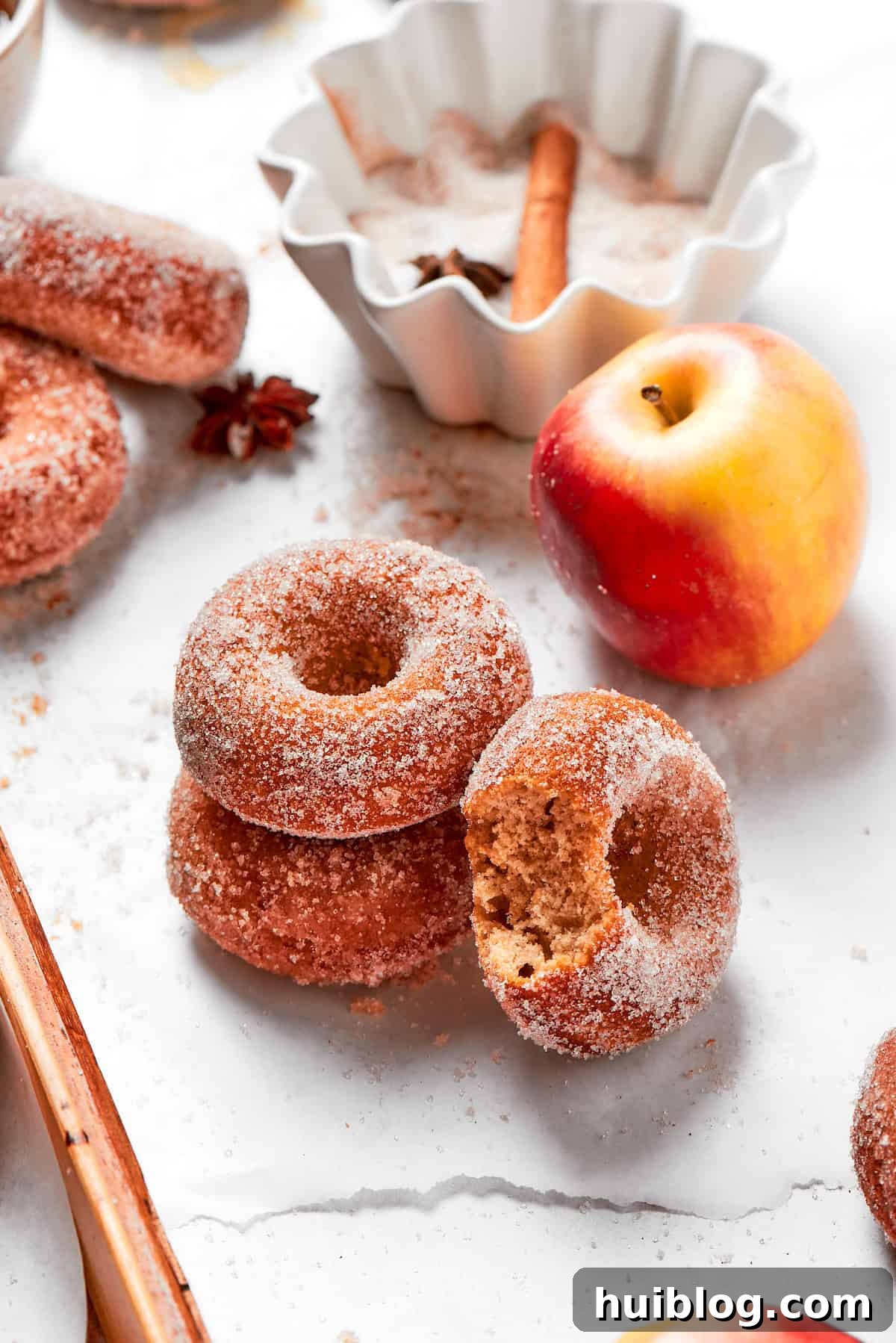 A little stack of apple cider donuts next to a crisp red apple, showcasing their spiced sugar coating.