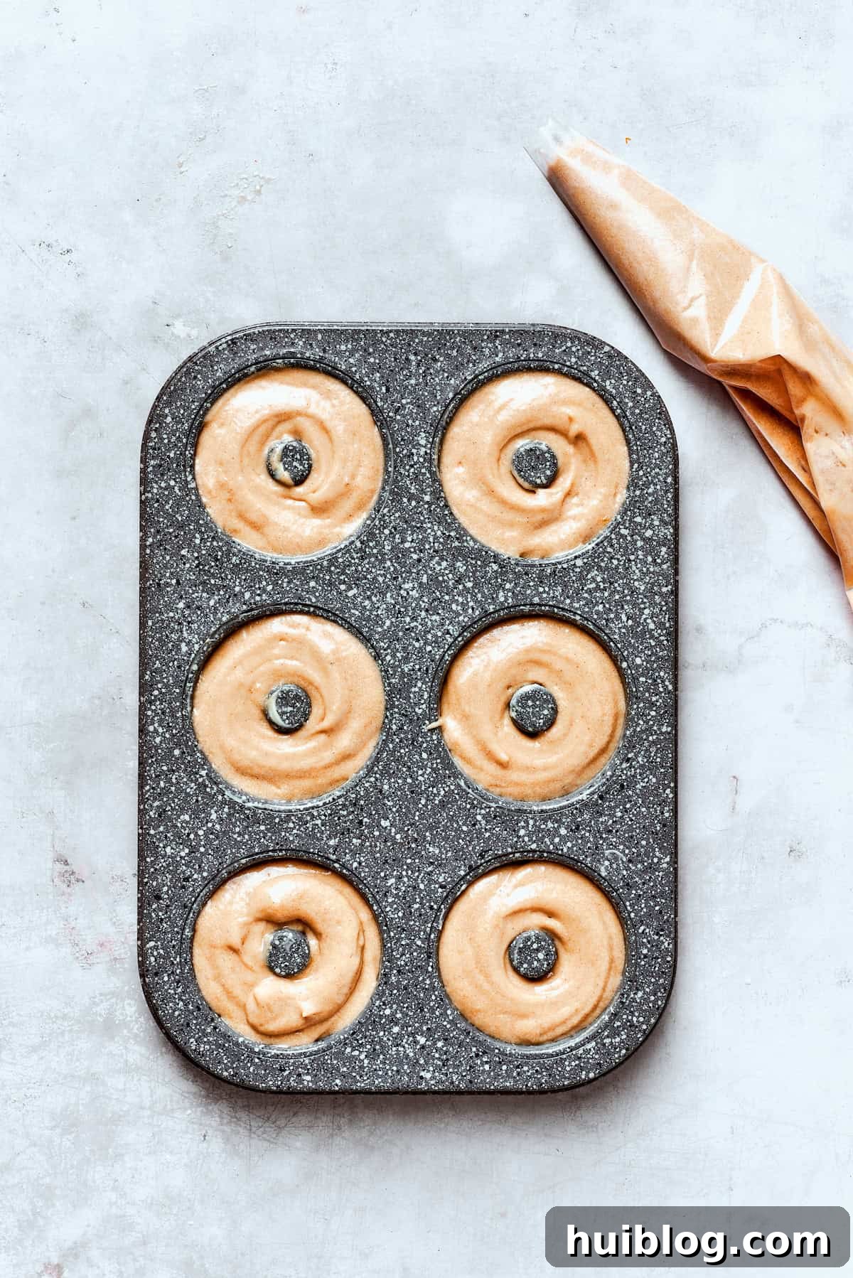 A piping bag filled with apple cider donut batter is used to neatly fill the wells of a donut pan.