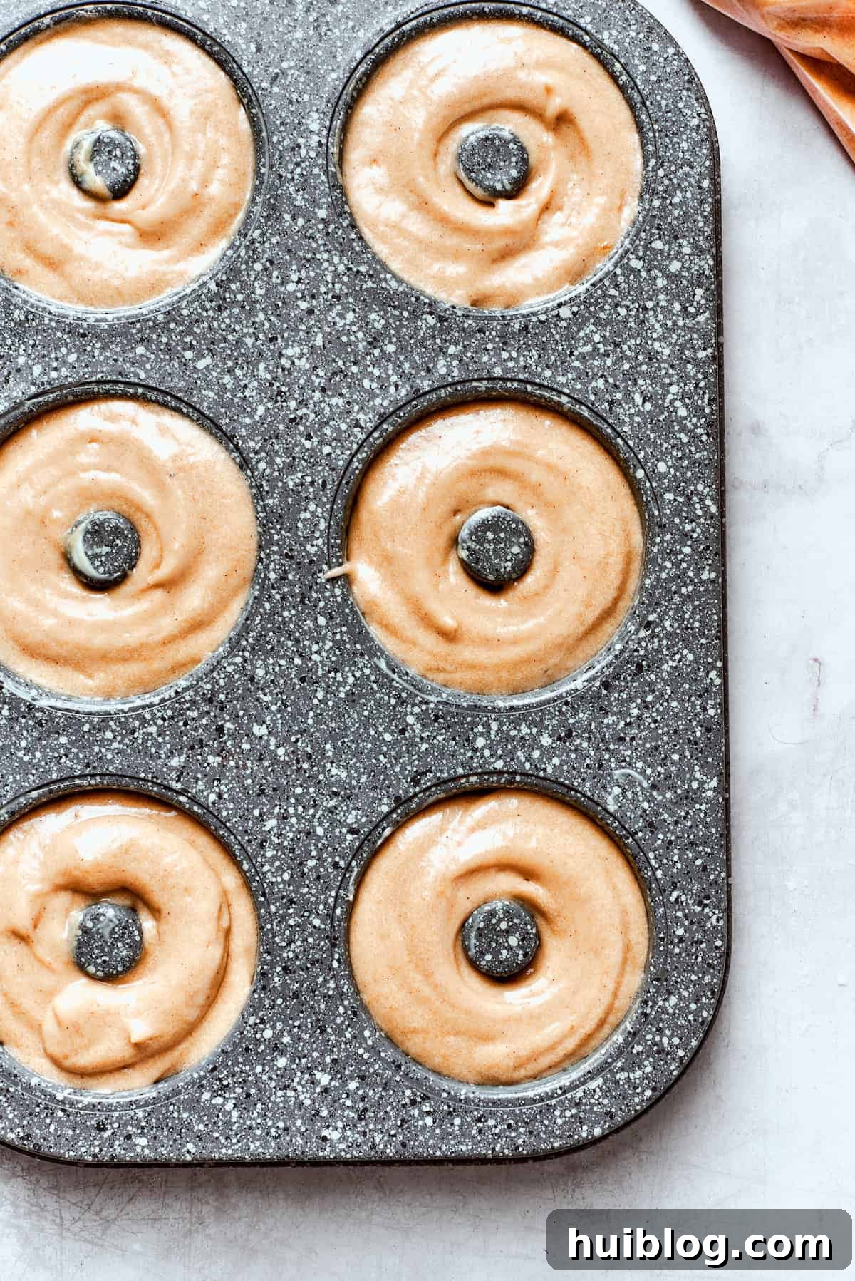 Close-up of apple cider donut batter expertly piped into a donut pan, filling each well about three-quarters full.