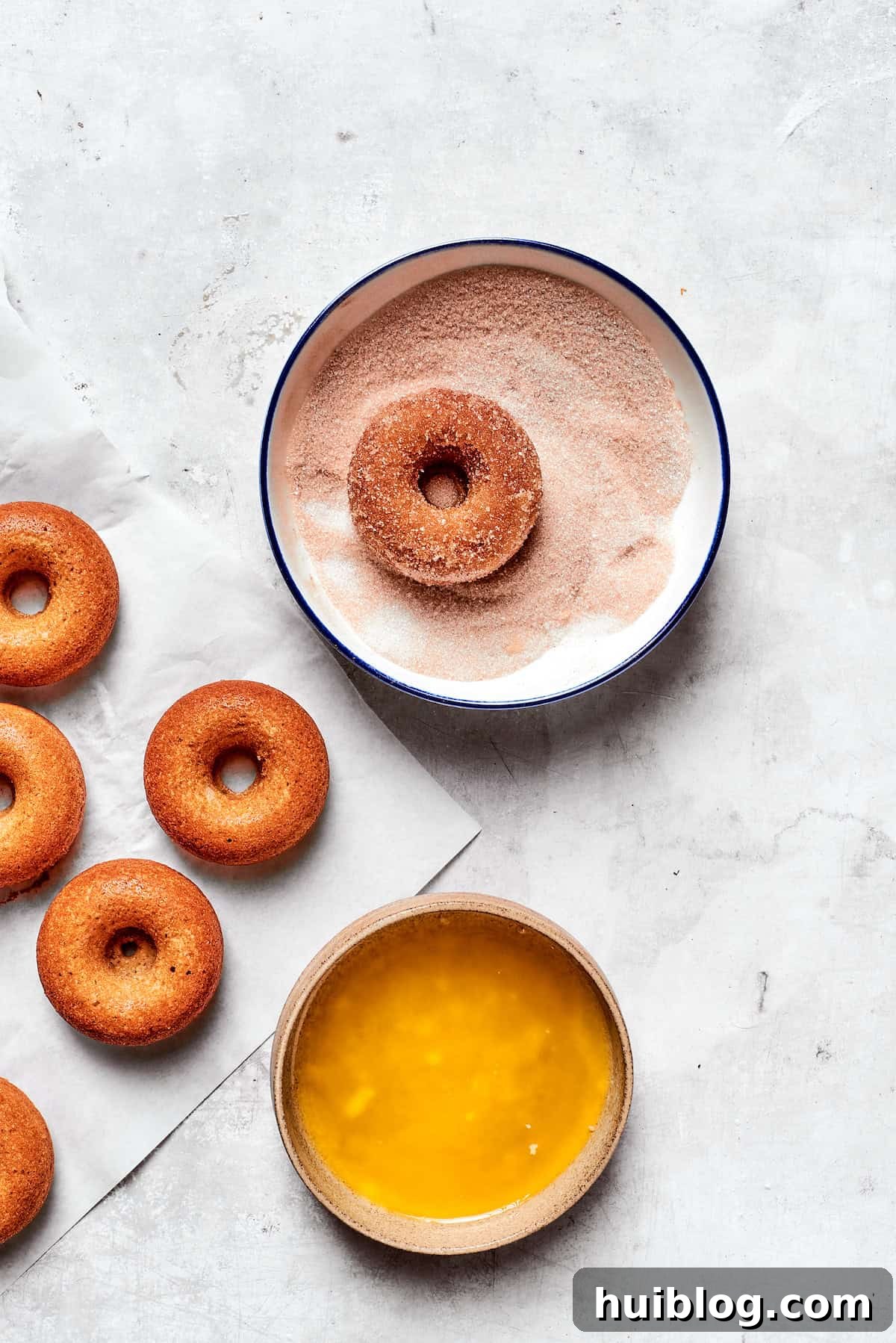 A freshly baked apple cider donut is first brushed with melted butter, then dipped and coated in a bowl of cinnamon sugar.