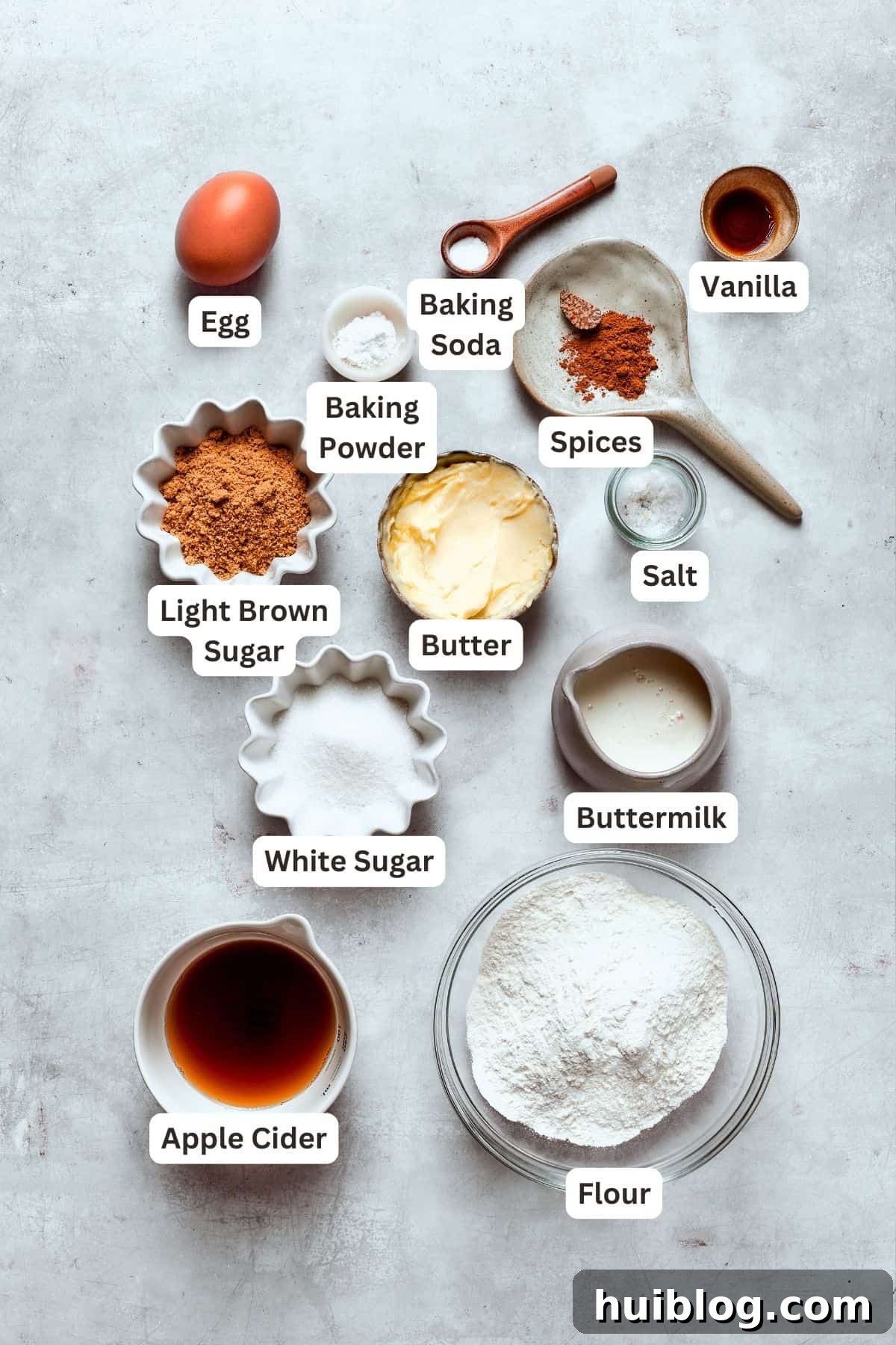 Various ingredients for apple cider donuts, including spices, apple cider, and butter, are neatly arranged with text labels.