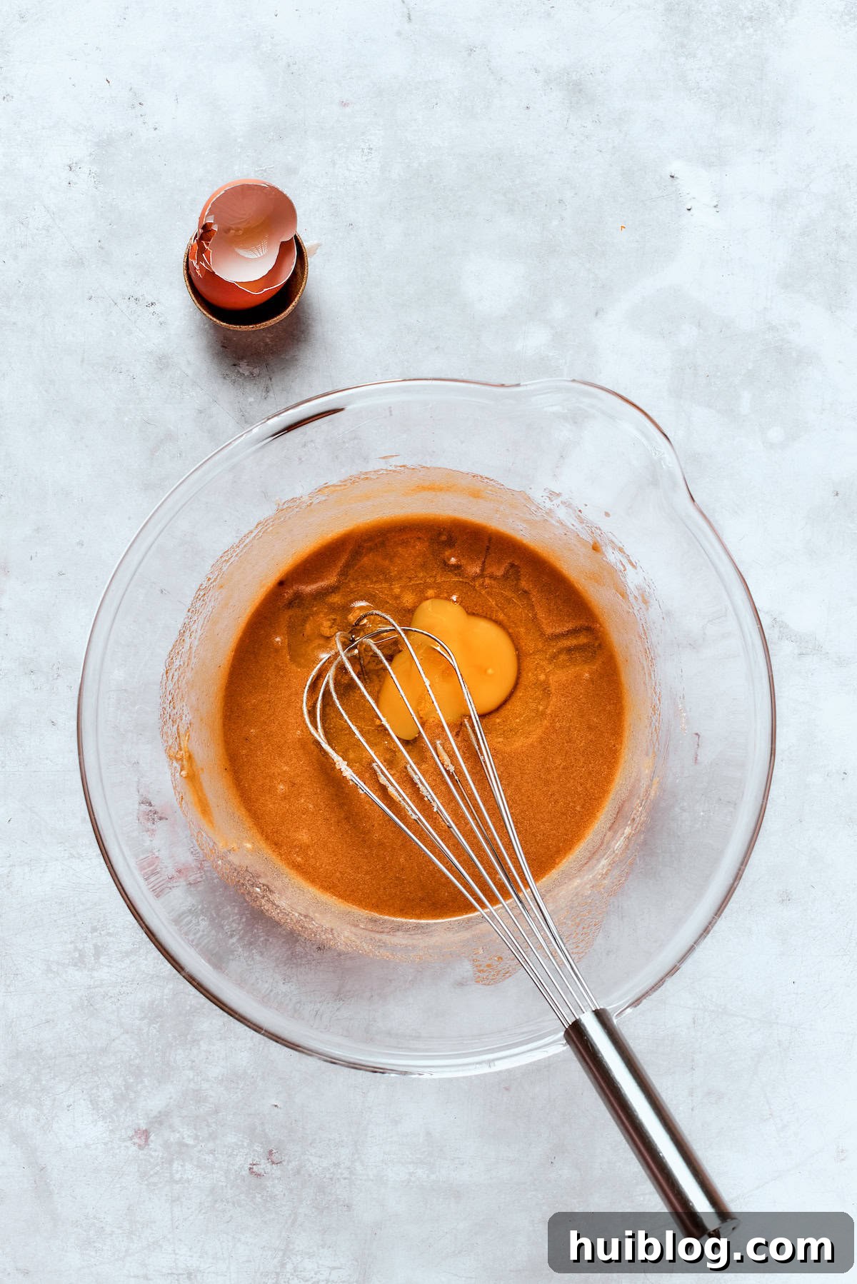 A whisk incorporates an egg and reduced apple cider into the butter and sugar mixture, creating a smooth wet batter.