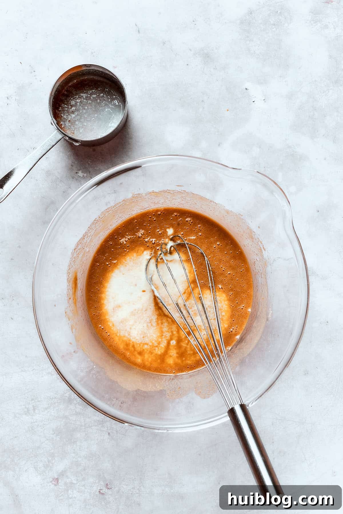 Buttermilk is gently whisked into a bowl of wet donut batter, contributing to its tender texture.