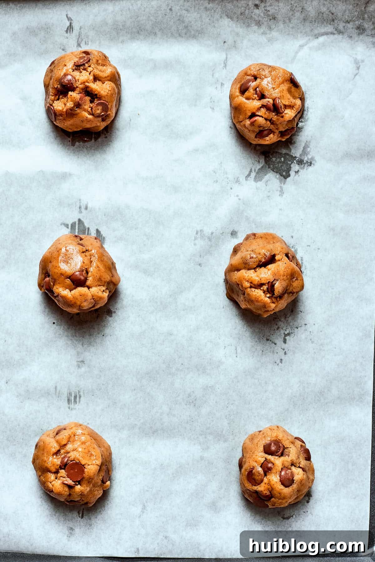 Evenly portioned balls of brown butter chocolate chip cookie dough resting on a parchment-lined baking sheet, ready for the oven.