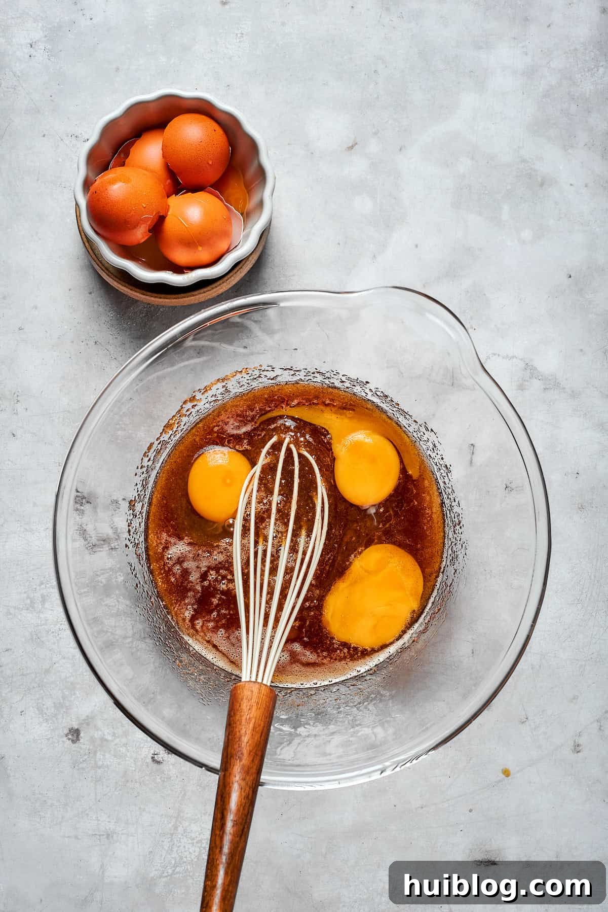 Two large eggs and one egg yolk being added to the creamy mixture of browned butter and sugars.