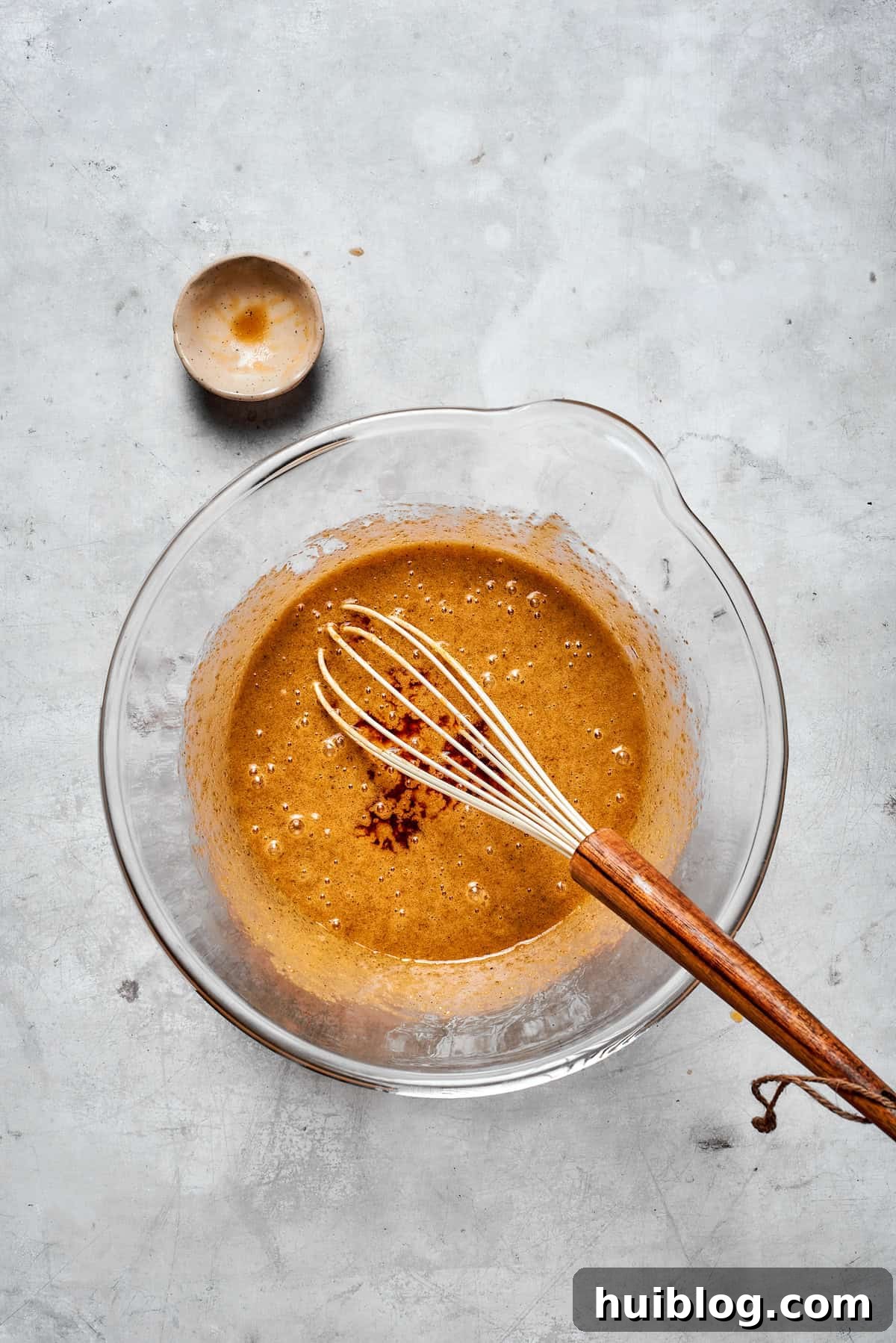 The cookie dough being vigorously whisked in a bowl to fully incorporate the eggs into the butter and sugar mixture.