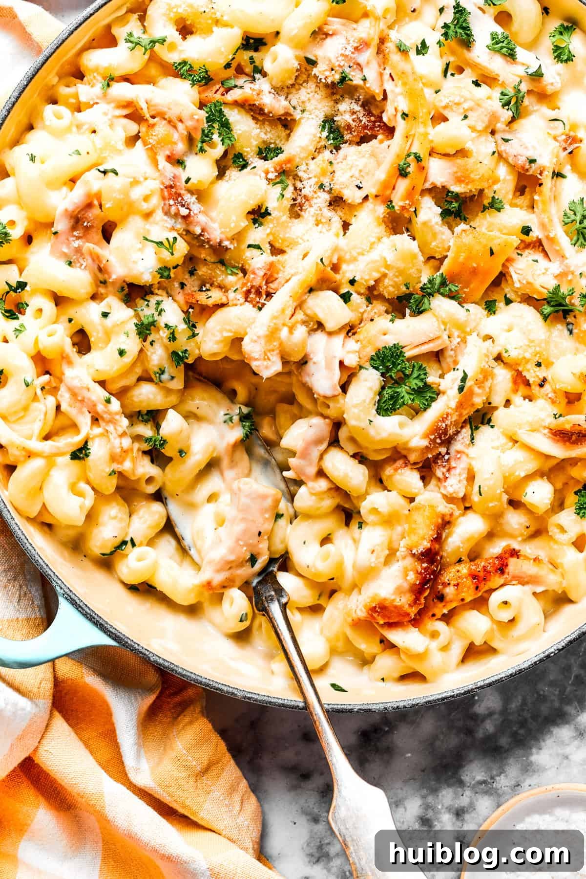 Indulge in this creamy garlic parmesan chicken pasta – a perfect blend of garlicky shredded chicken and luscious pasta, perfect for any night. A close-up of creamy garlic parmesan chicken pasta in a cast iron skillet, with a serving spoon nestled in the rich sauce and tender pasta.