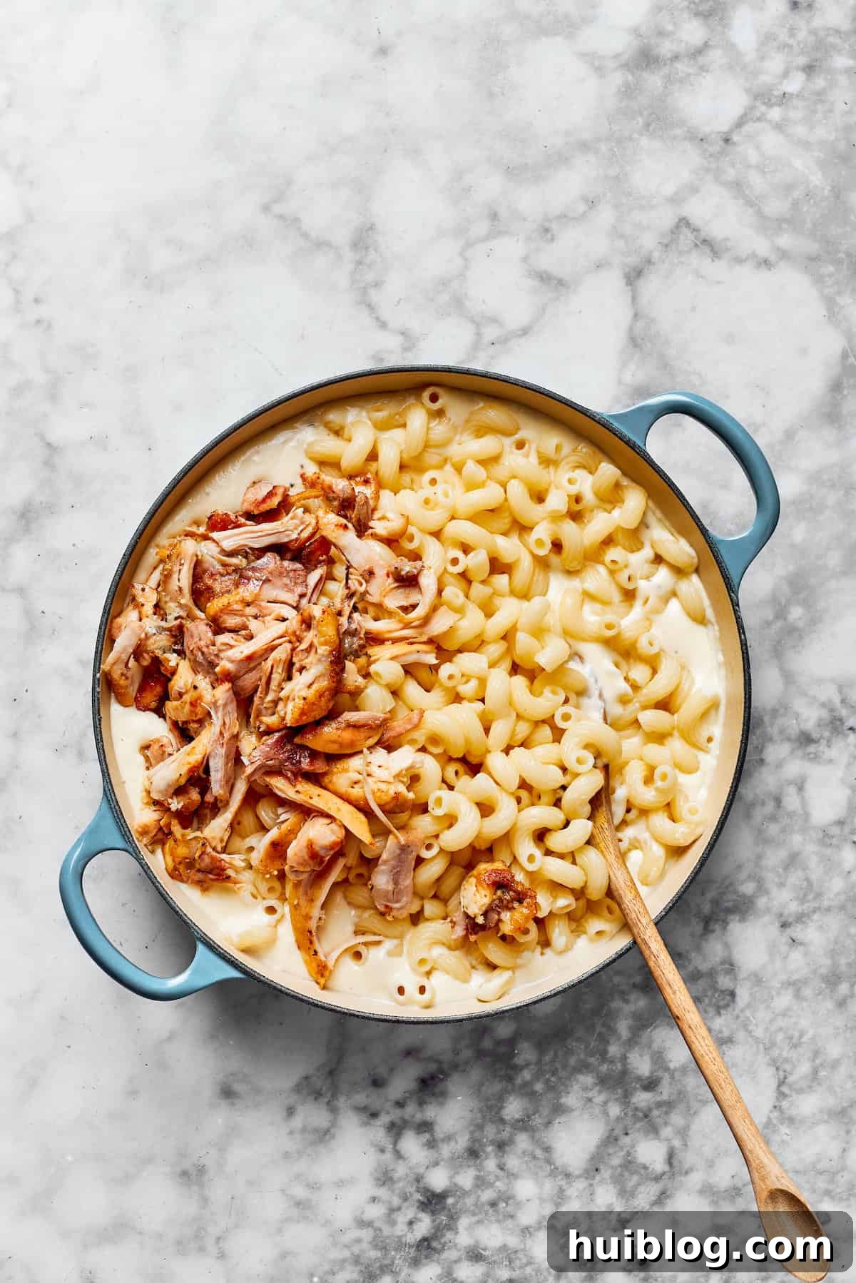 Add chicken & cooked pasta. Cooked pasta and shredded chicken being stirred into a large saucepan of creamy garlic parmesan sauce, uniting all the elements of the dish.