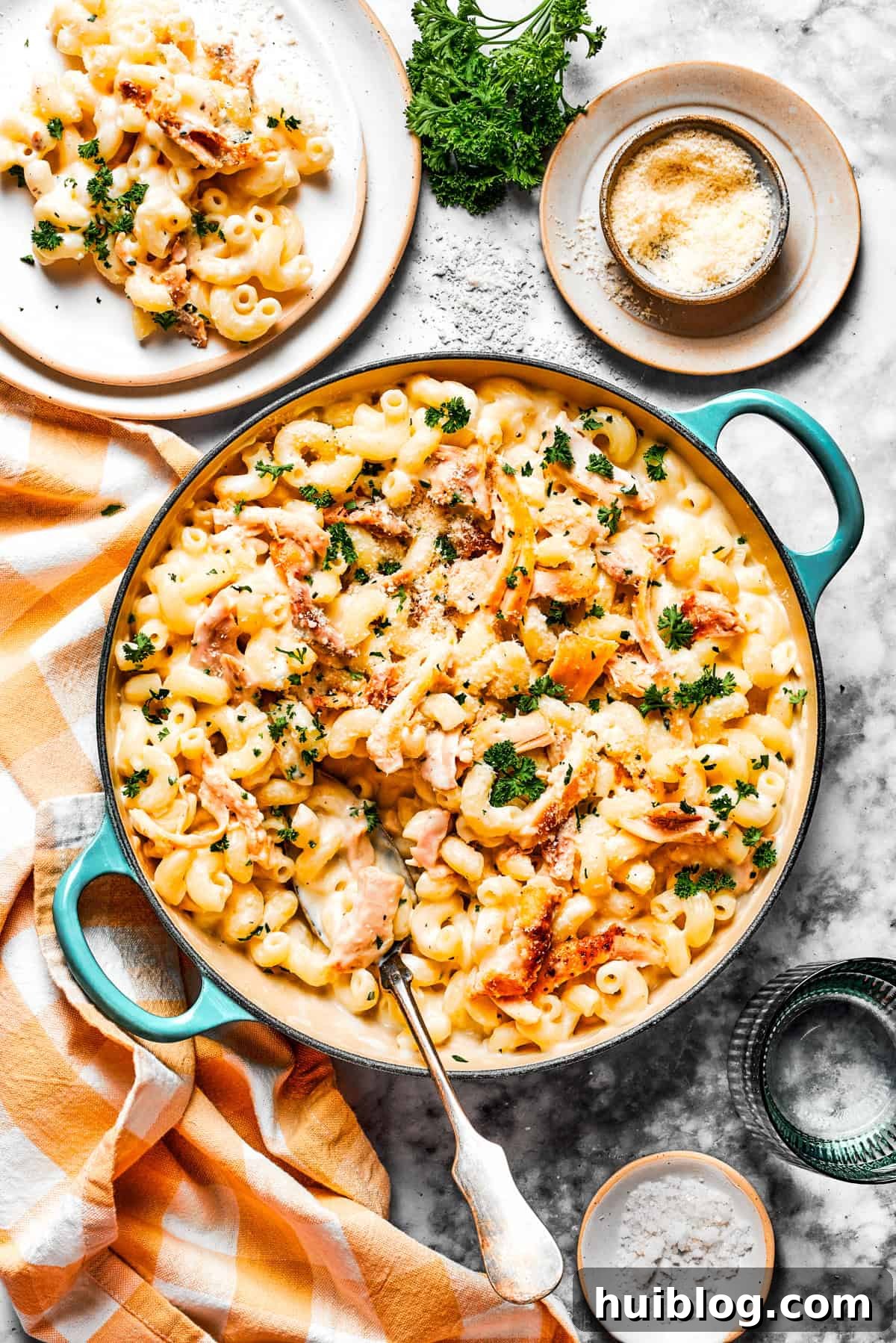 Overhead photo of parmesan chicken pasta in a pot, with a serving of the pasta on a dinner plate set next to the pot. An overhead view of creamy garlic parmesan chicken pasta in a large pot, with a separate serving on a white dinner plate next to it, ready to be enjoyed.