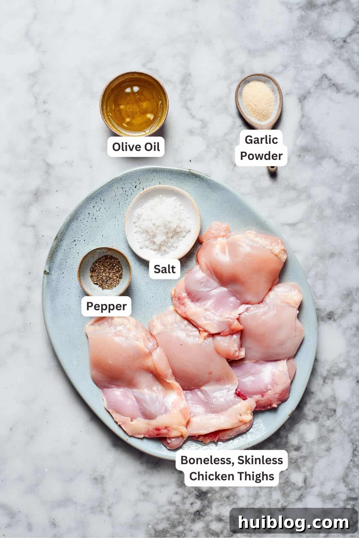 Roasted chicken ingredients A selection of ingredients for roasting chicken, including boneless skinless chicken thighs, olive oil, garlic powder, salt, and black pepper, arranged on a wooden board.