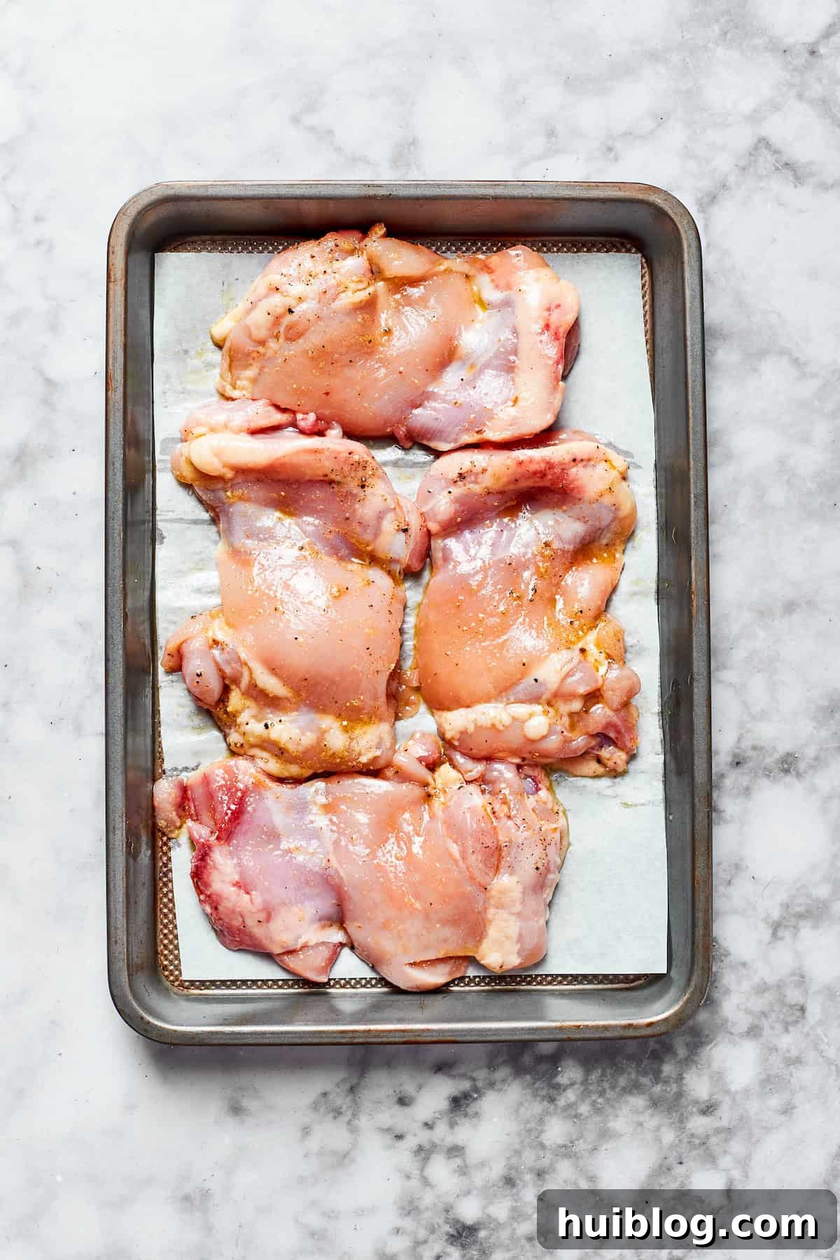 Season & Roast the chicken. Raw chicken thighs seasoned with olive oil, salt, pepper, and garlic powder, arranged in a single layer on a parchment-lined baking sheet, ready for roasting.