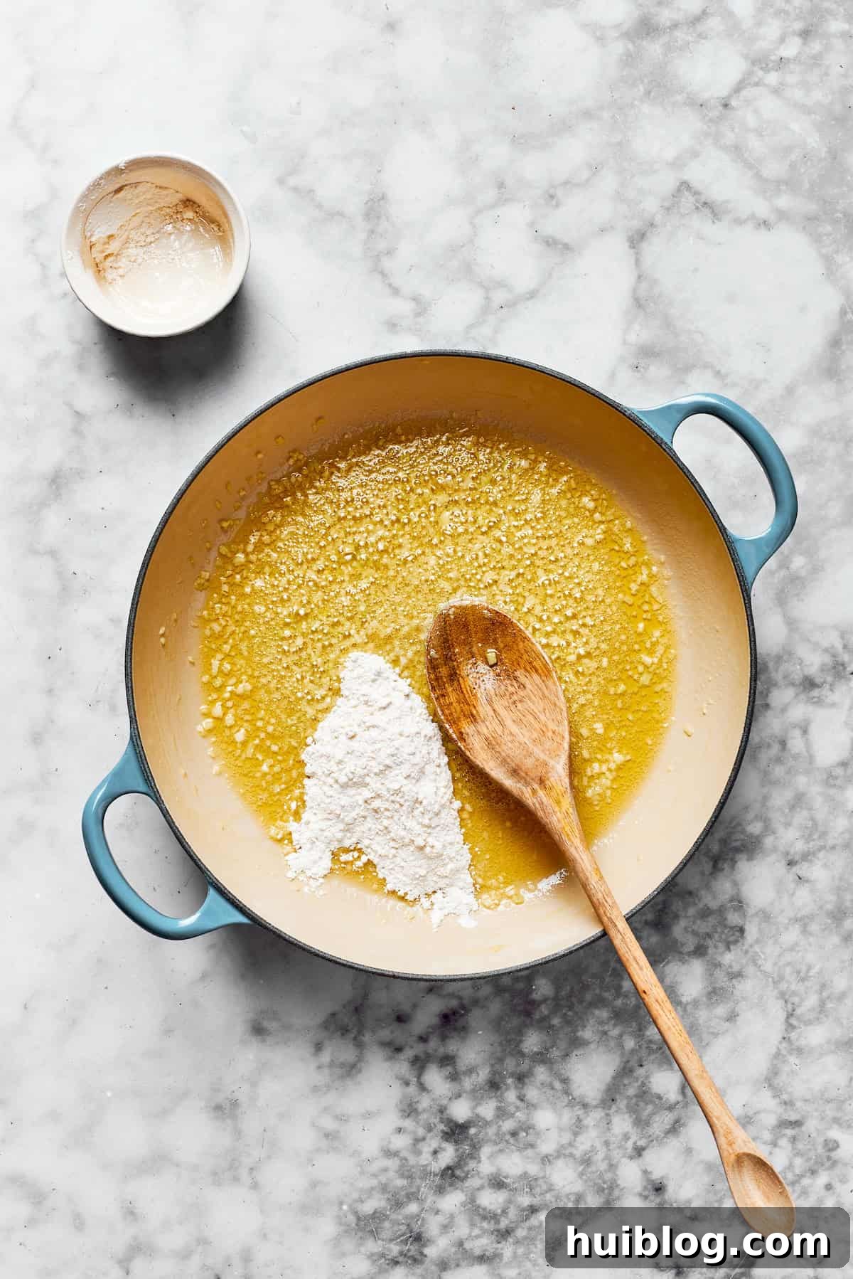 Saute garlic, add flour. Melted butter and minced garlic simmering in a large saucepan, with all-purpose flour added to create a roux for the creamy sauce.
