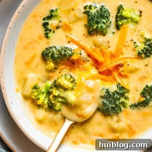 Bowl of broccoli cheese soup garnished with shredded cheese and broccoli florets.