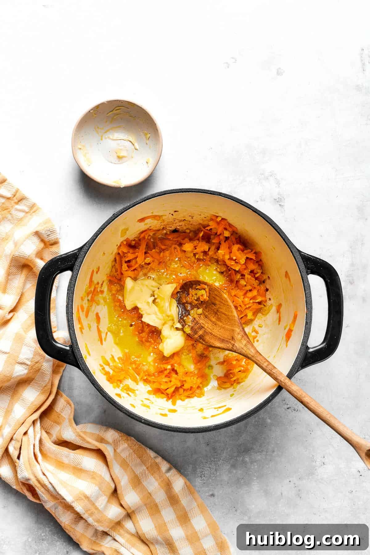Adding unsalted butter to a pot with sautéed carrots and onions.