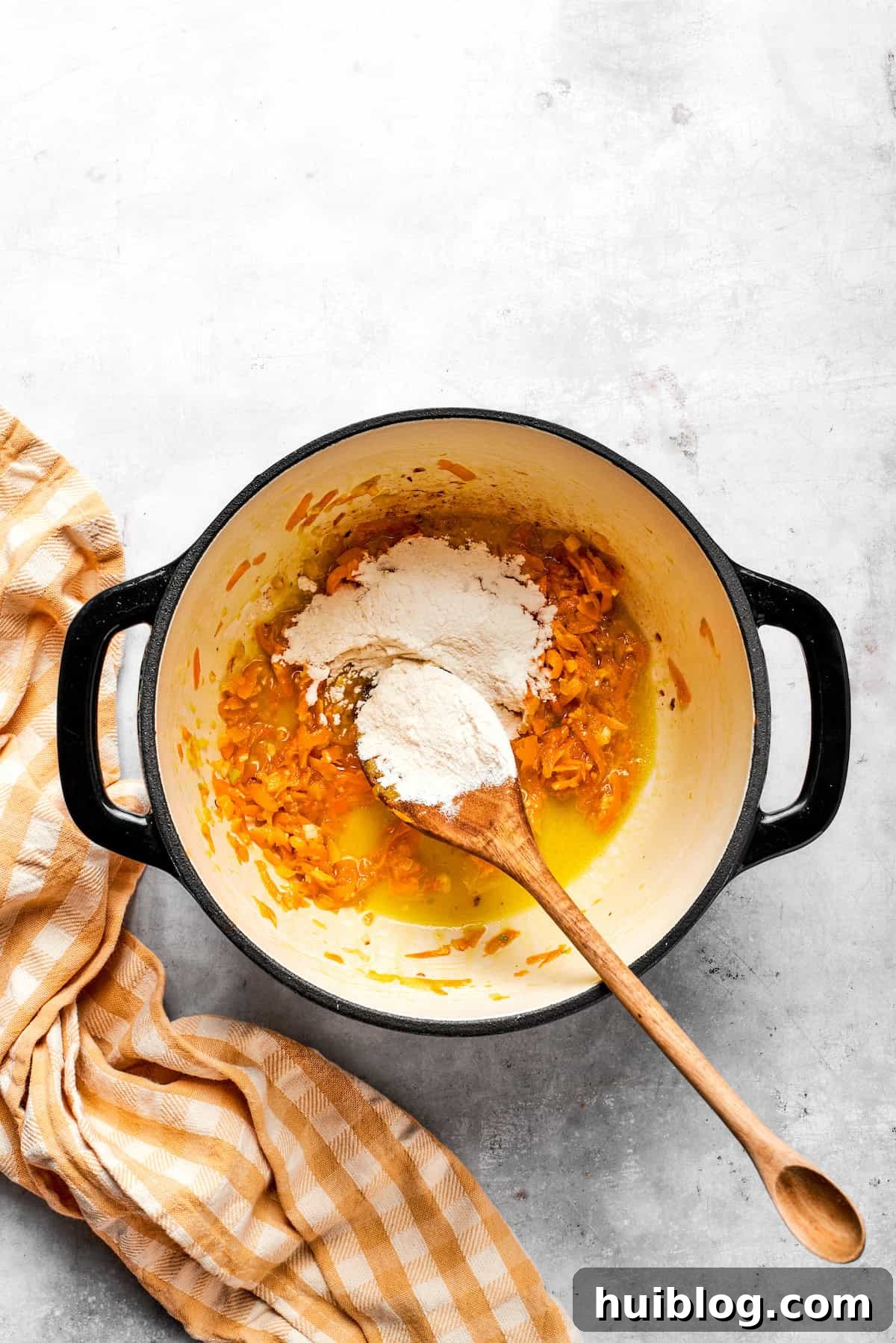 Sprinkling all-purpose flour into a pot with melted butter and vegetables, preparing for the roux.
