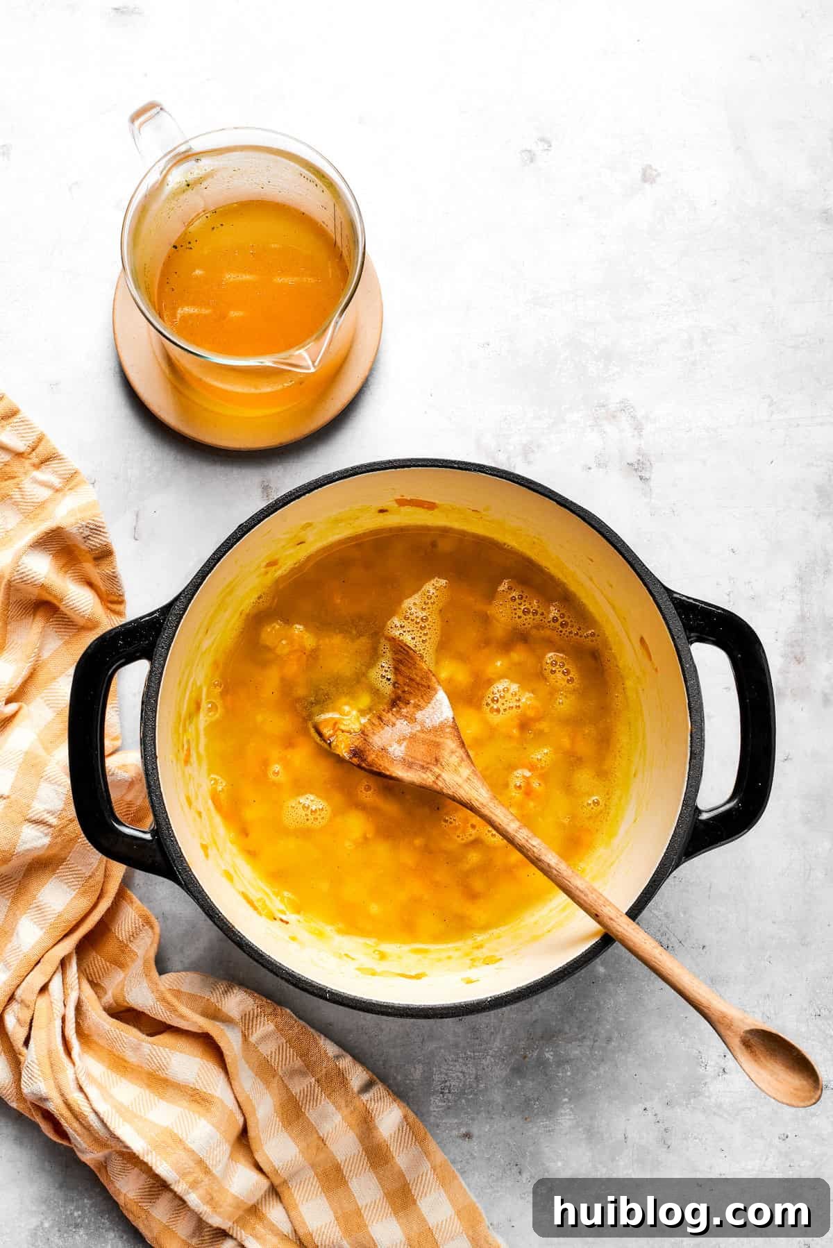 Pouring vegetable broth into a pot with the roux and vegetables, beginning to thicken the soup base.