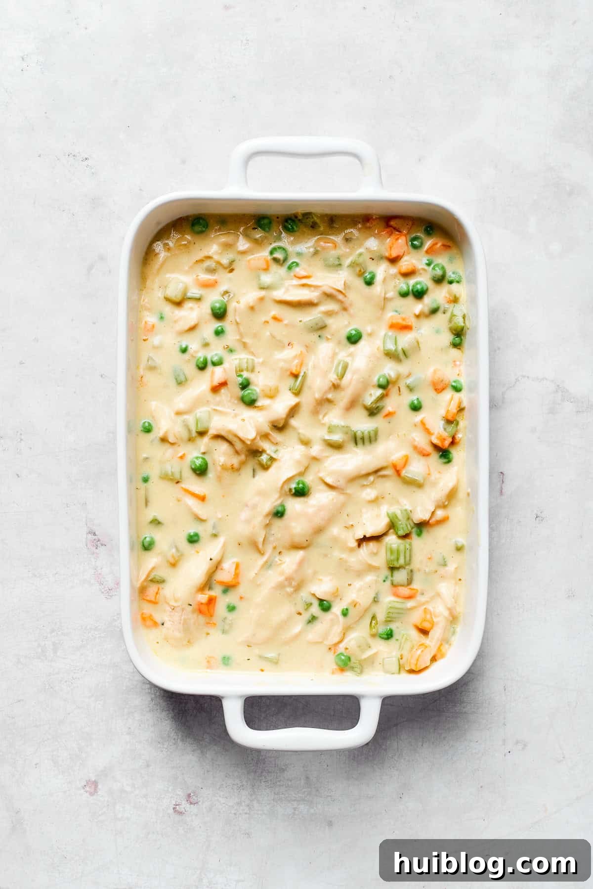 This chicken stuffing casserole features tender chicken filling with veggies topped with classic stuffing. An easy recipe baked until golden! Spreading the creamy chicken filling evenly in a baking dish.
