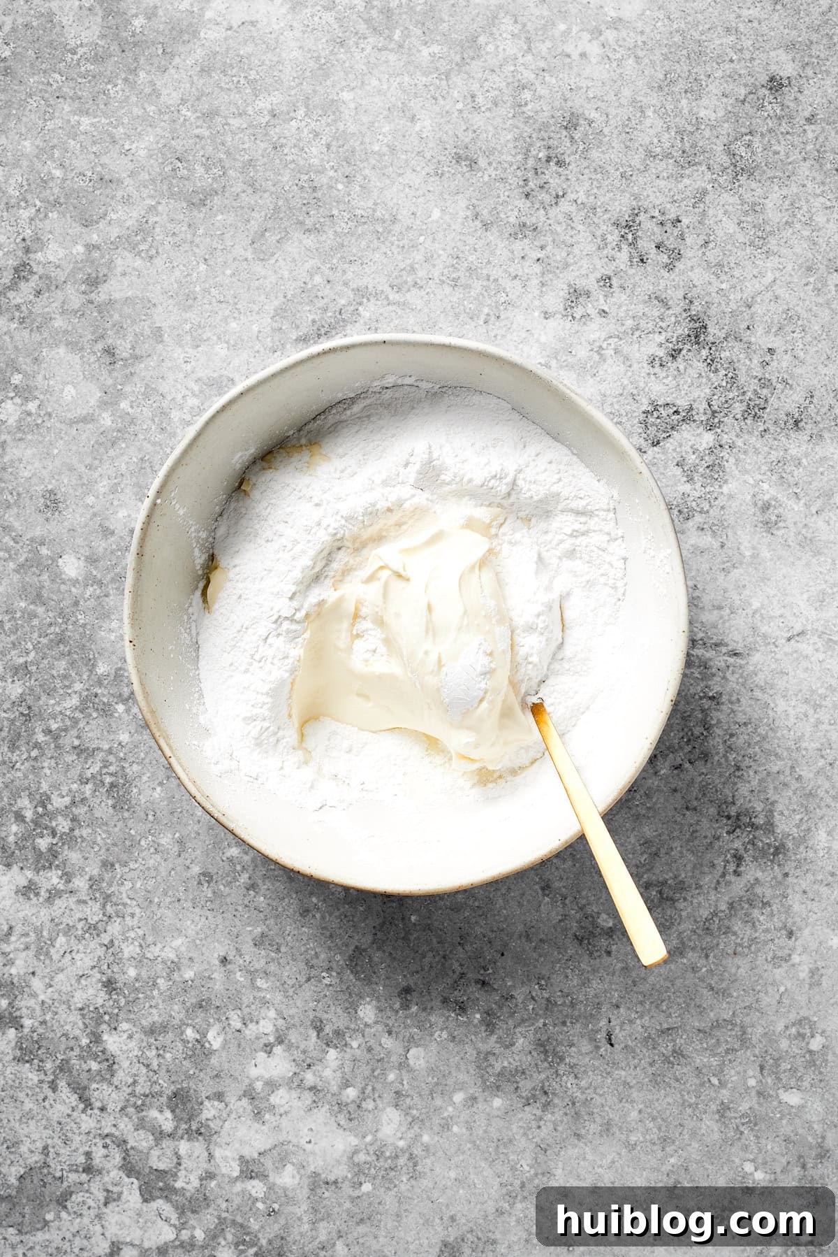 Cream cheese and powdered sugar are mixed together in a bowl for the frosting.