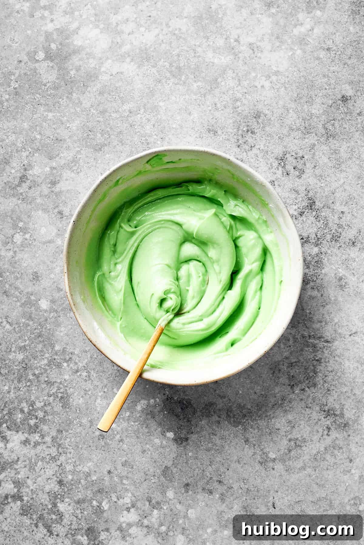A spoon stirs green food coloring into the icing, turning it vibrant green.