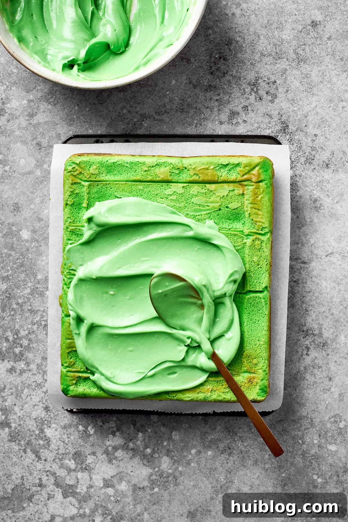 Vibrant green icing is spread generously on top of a baked Grinch cake.