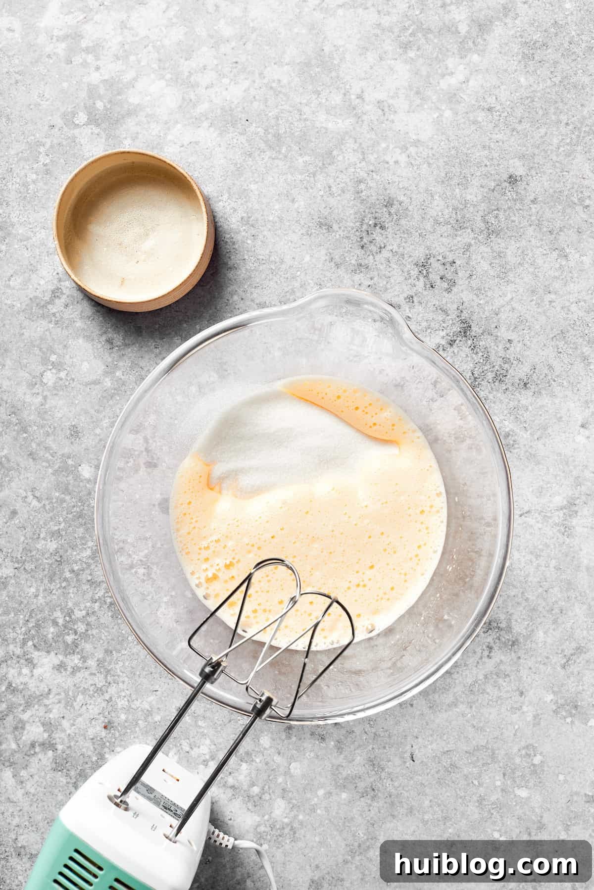 Granulated sugar being beaten into the whisked eggs.
