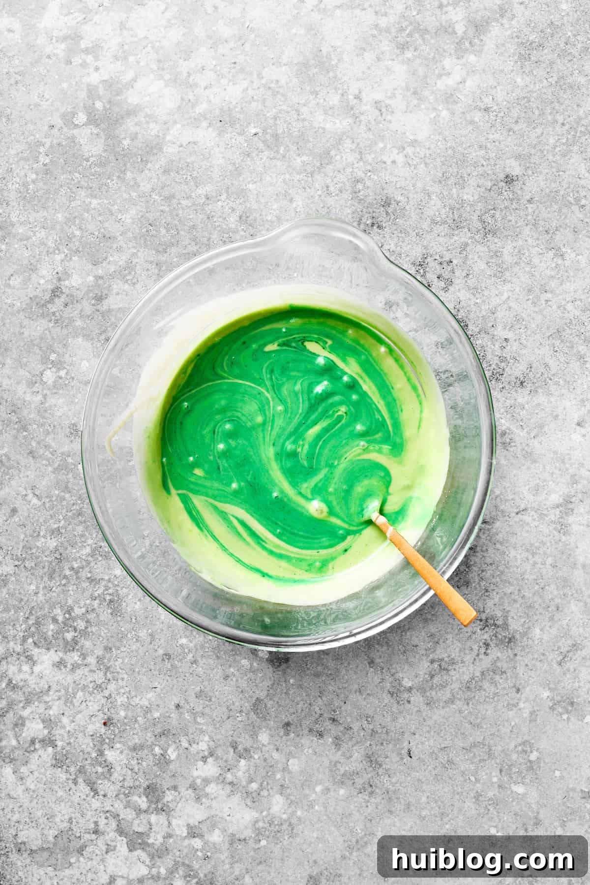 The grinch cake batter turns green as green food coloring is stirred in.