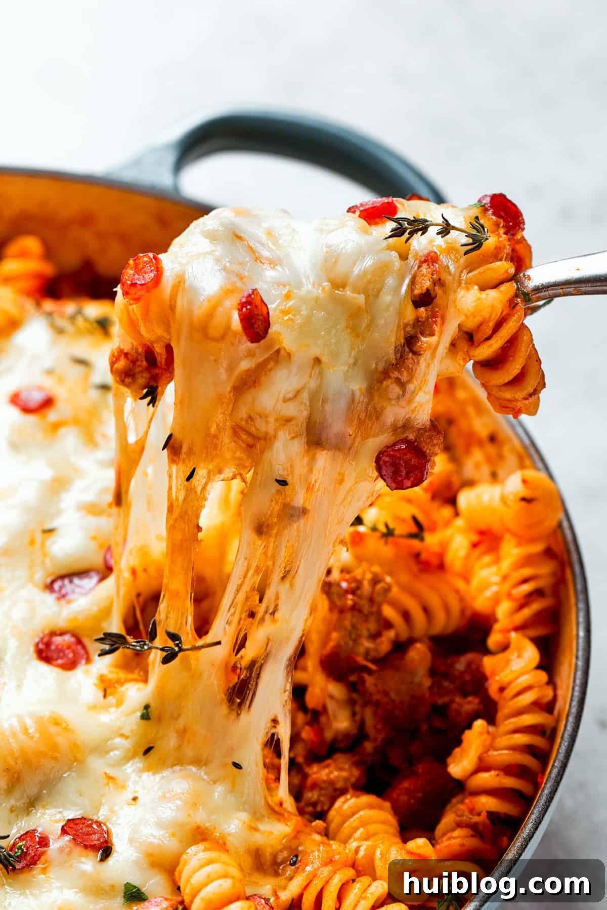 A close-up shot capturing a fork pulling a string of melted cheese and pasta from a baking dish of pizza pasta.