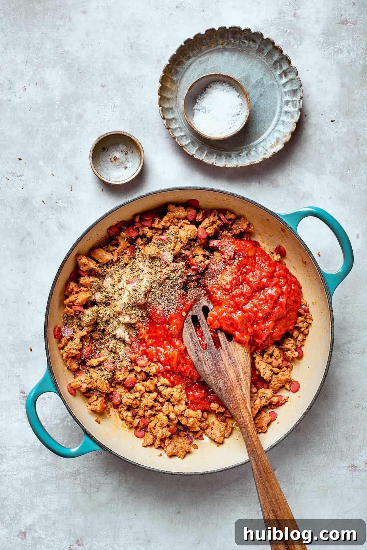 Zesty tomato sauce is being stirred into the skillet with cooked sausage and pepperoni, creating a rich base.