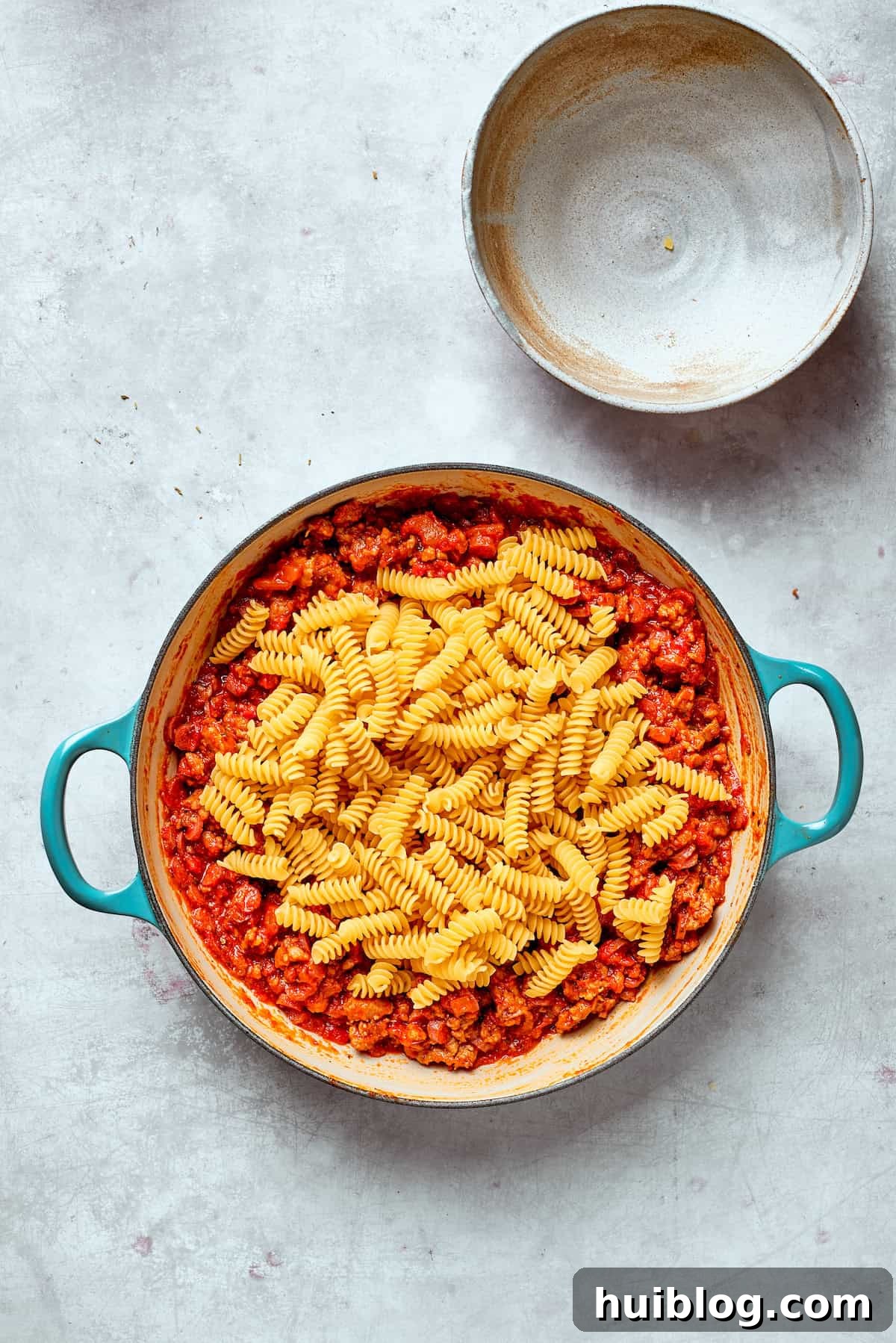 Uncooked rotini pasta is gently poured into the skillet, joining the rich tomato sauce and meat mixture.