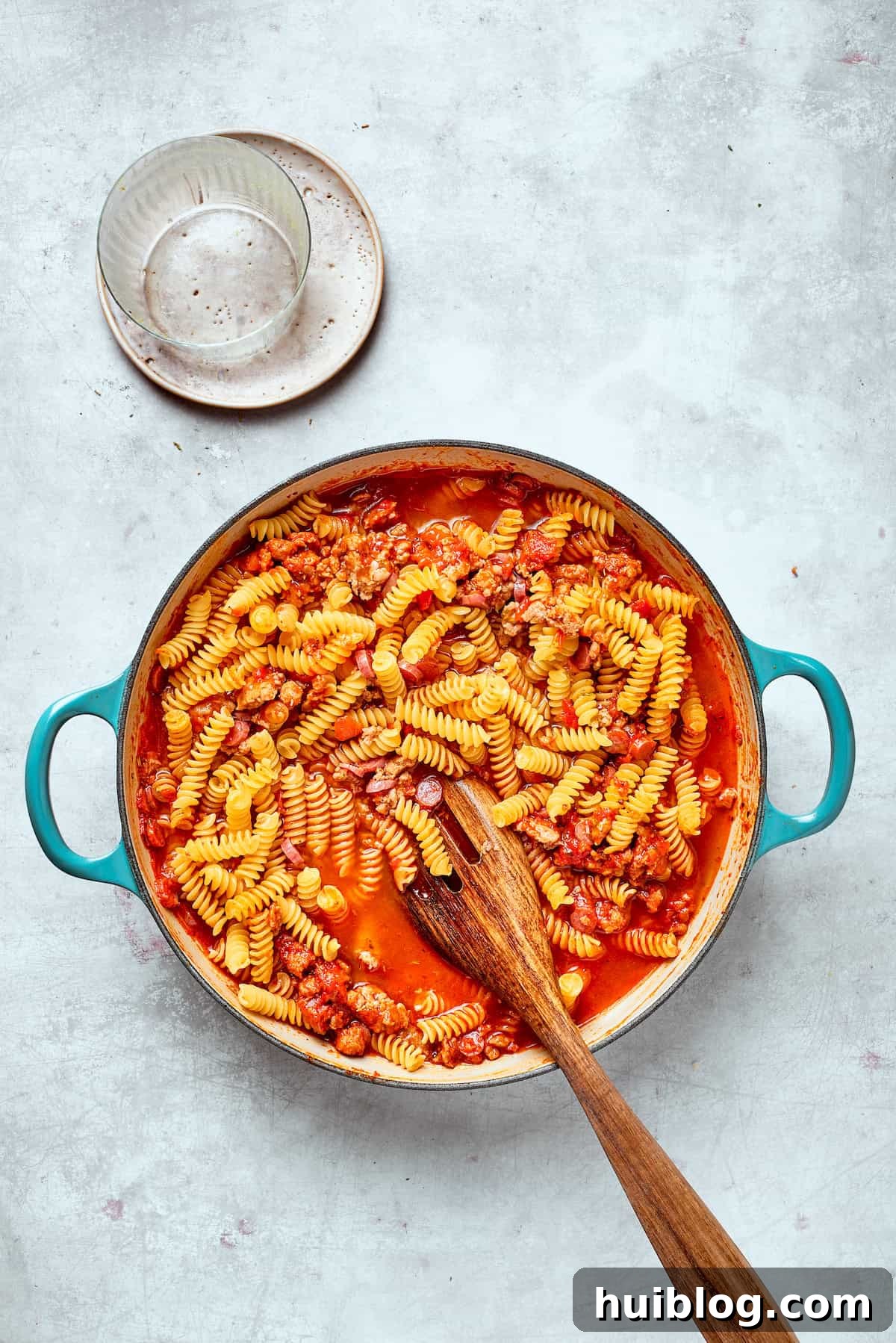 A spoon gently mixes the rotini pasta into the savory sauce and broth, ensuring everything is well combined.