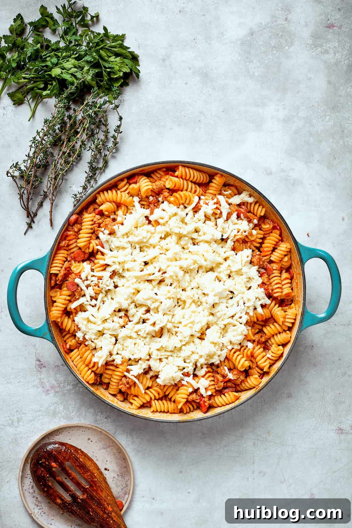 Generous handfuls of shredded mozzarella cheese are sprinkled over the hot pizza pasta, ready to melt.