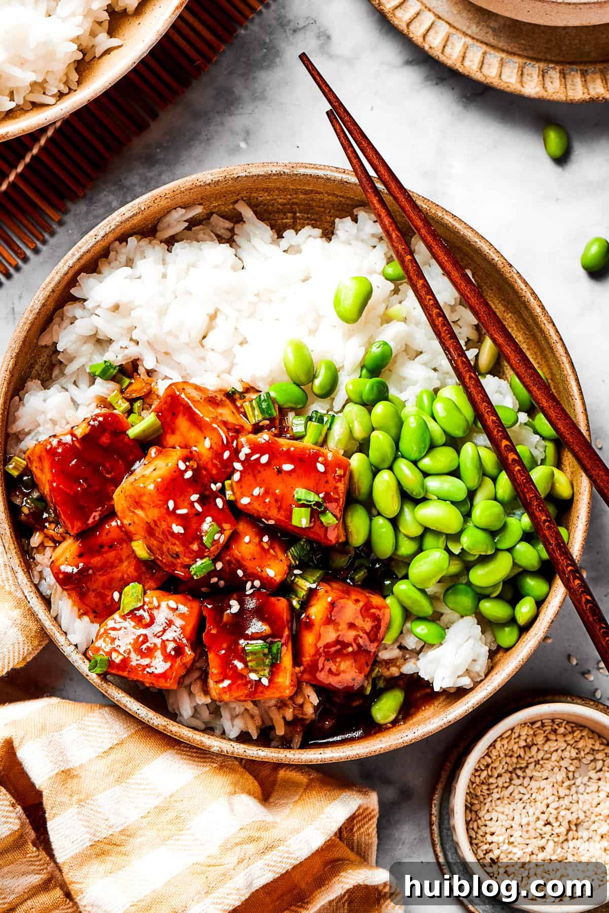 A beautifully arranged bowl of white rice topped with perfectly cubed, glazed teriyaki salmon and bright green edamame beans, ready to be enjoyed.
