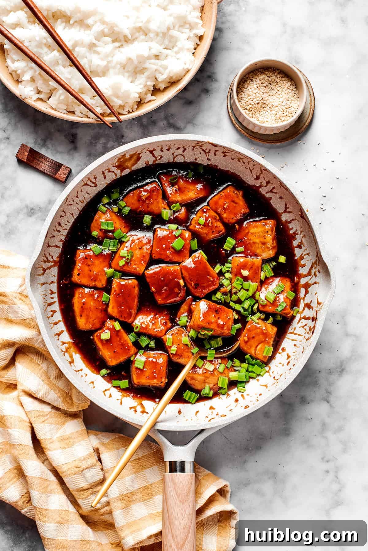 A large skillet filled with perfectly glazed teriyaki salmon chunks, alongside a bowl of steamed white rice, presenting a complete and enticing meal.