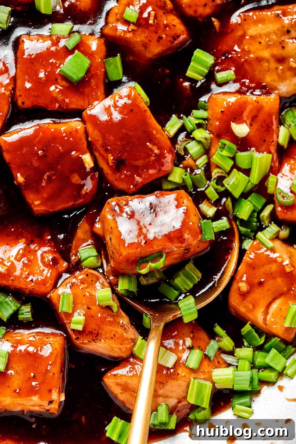 A close-up shot of a spoon scooping into a serving of perfectly cooked, glazed teriyaki salmon, showing its tender texture and glossy sauce.