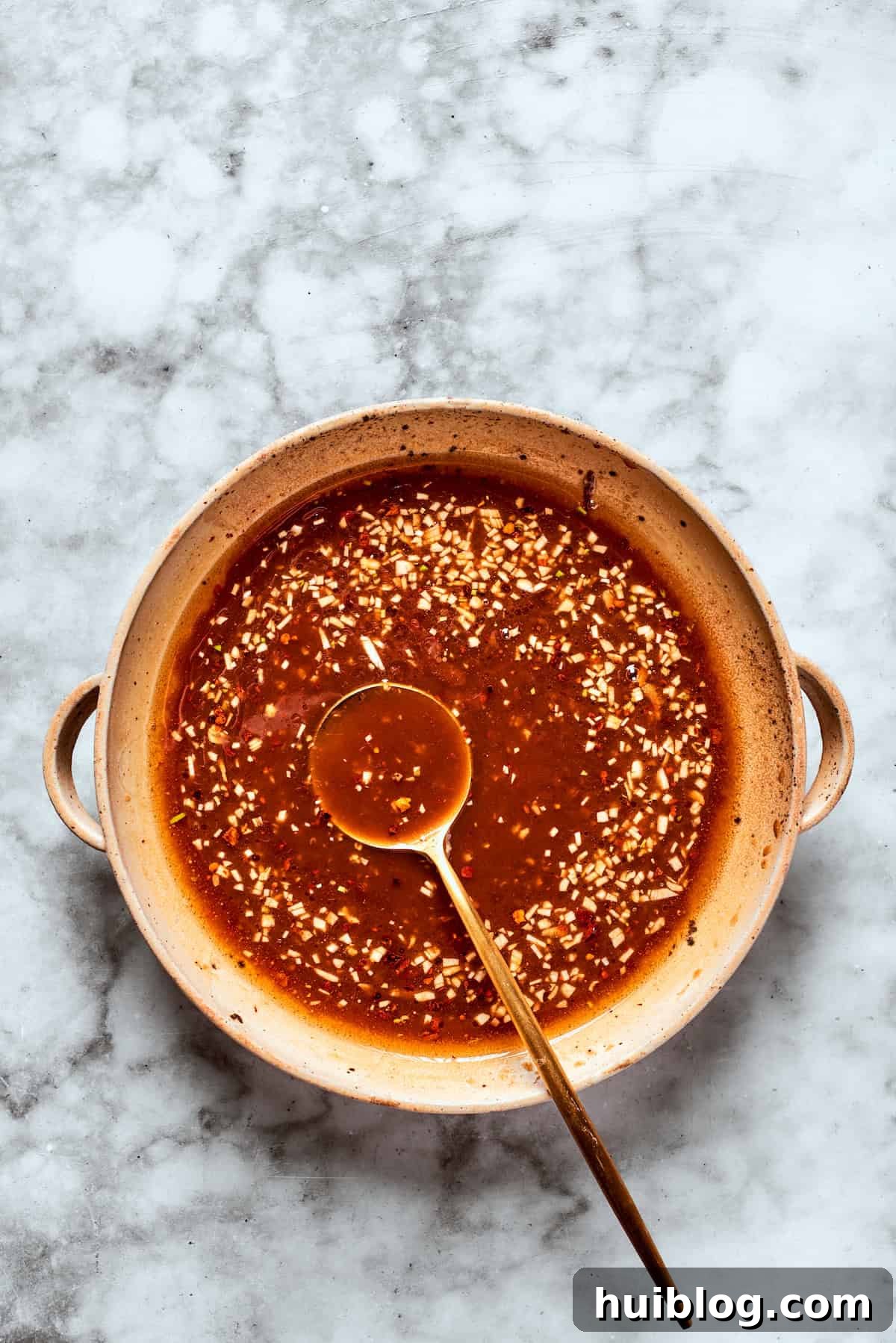 A spoon tests the consistency of the teriyaki sauce as it thickens in a saucepan over heat.