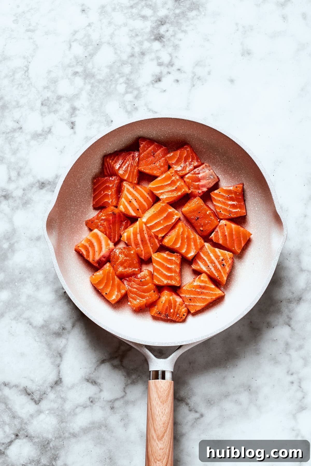 Cubed salmon pieces are searing in a hot skillet, developing a golden crust.