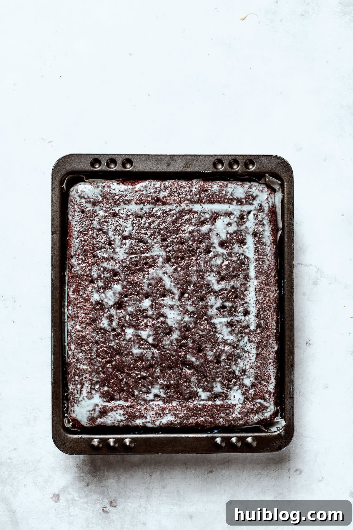 Sweetened condensed milk soaking into a chocolate cake, filling the poked holes.