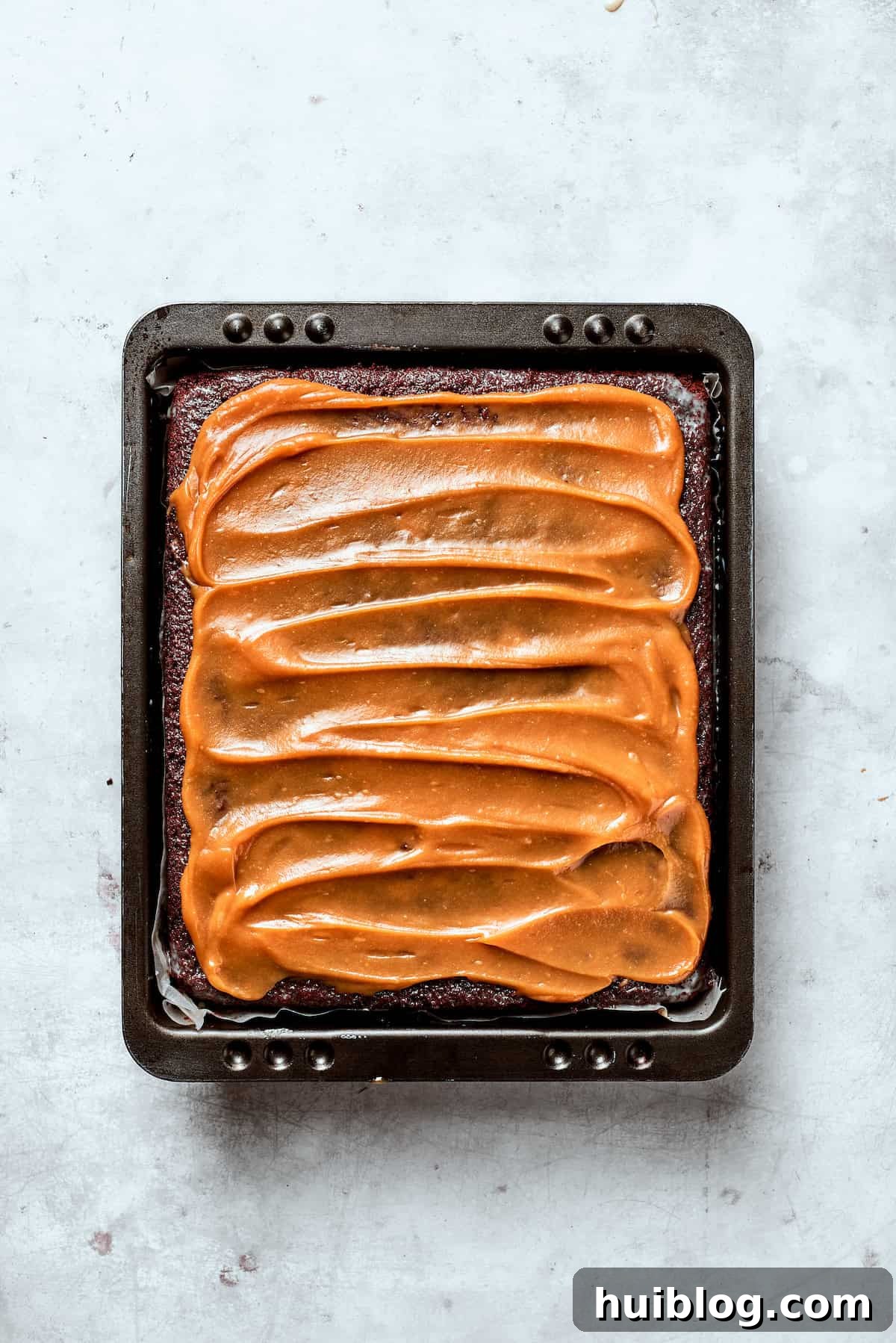 Smooth, rich caramel sauce being spread evenly over the top of a chocolate cake.