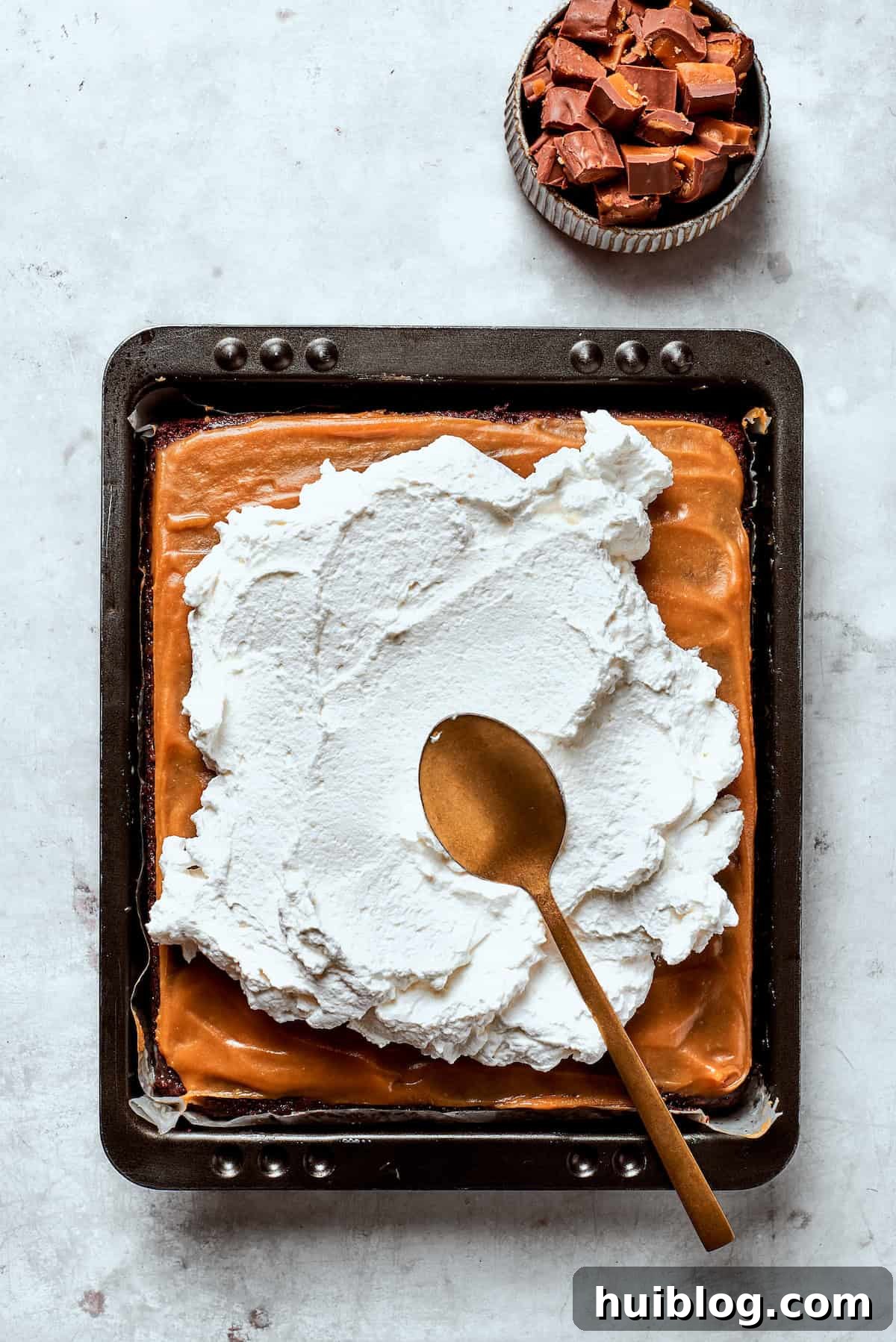 Fluffy Cool Whip being gently spread over a caramel-topped chocolate cake.
