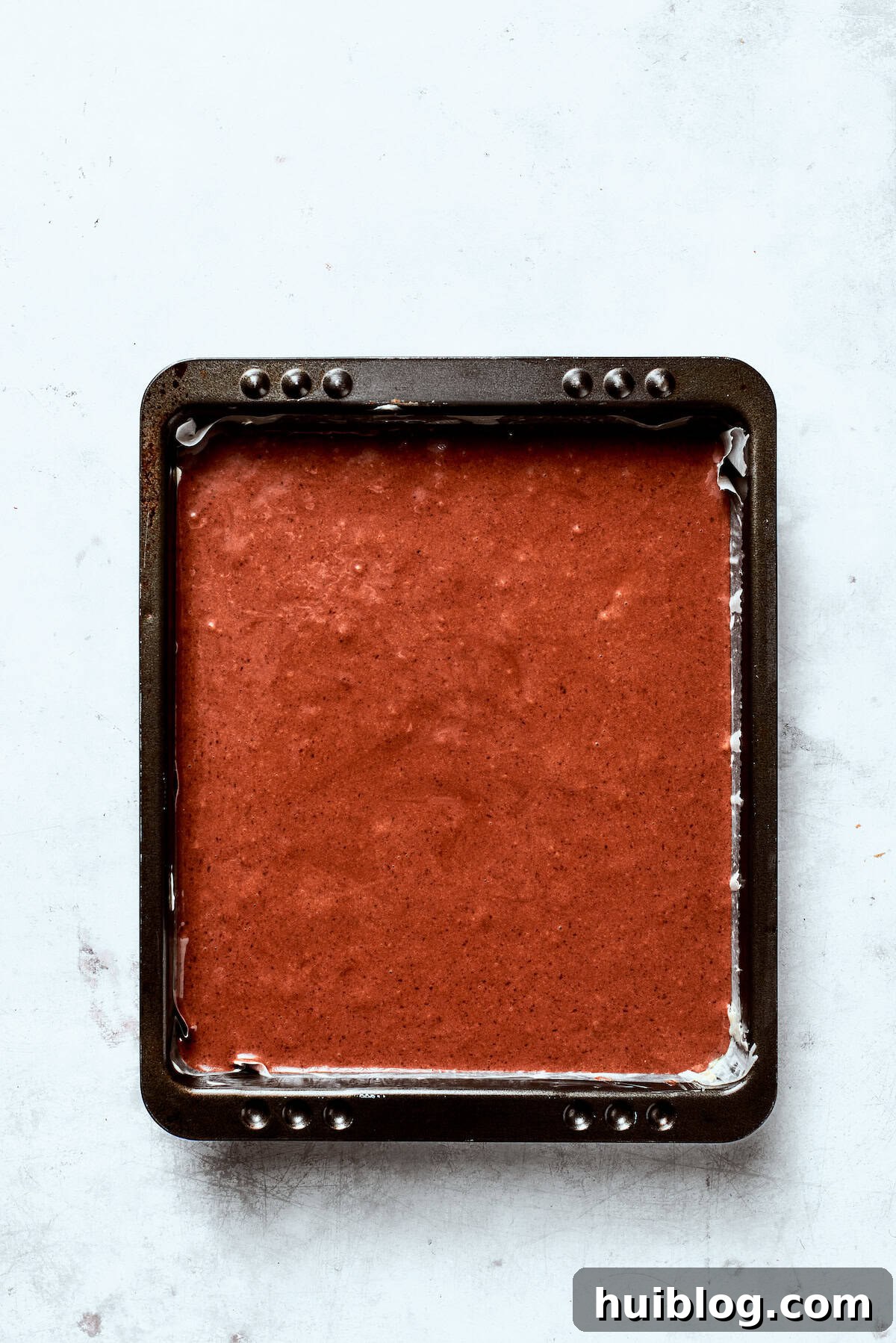 Chocolate cake batter being poured into a cake tin, ready for baking.