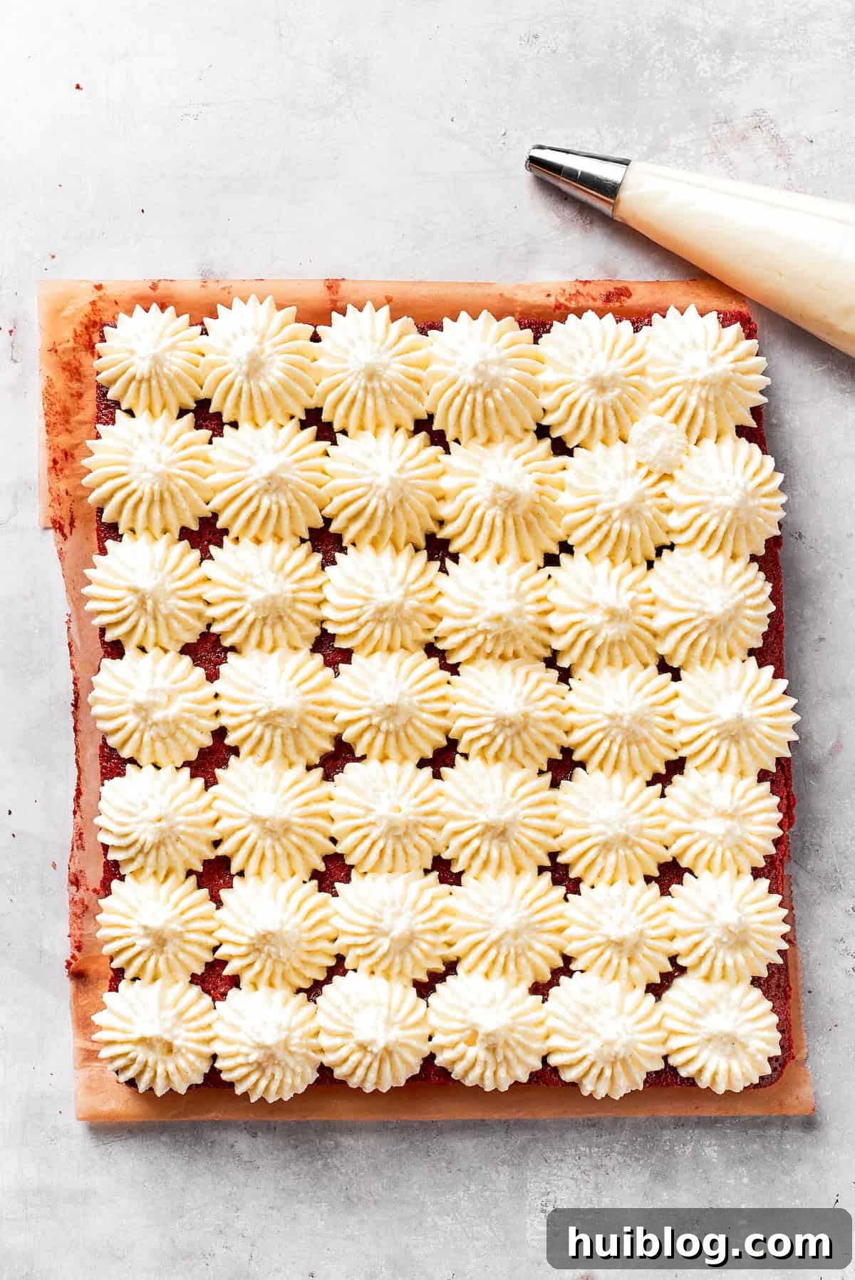Cream cheese frosting piped onto red velvet brownies.