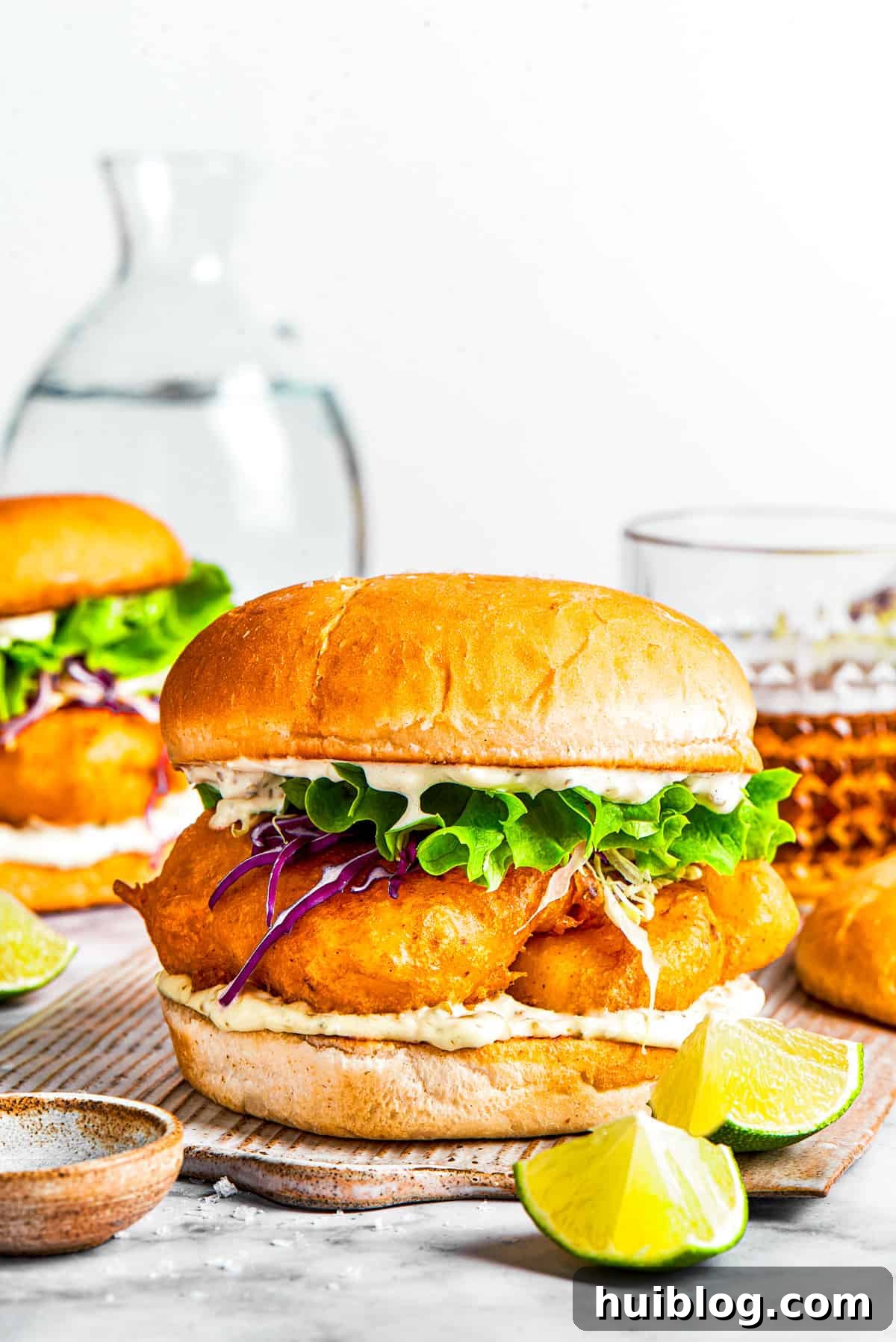 This crispy, crunchy fish sandwich is served on toasty sweet rolls with lemony tartar sauce and a squeeze of lime! It's quick and easy to make! A perfectly assembled crispy fish sandwich, featuring a golden-fried fish fillet, crisp lettuce, and creamy tartar sauce, nestled in a toasted sweet bun.