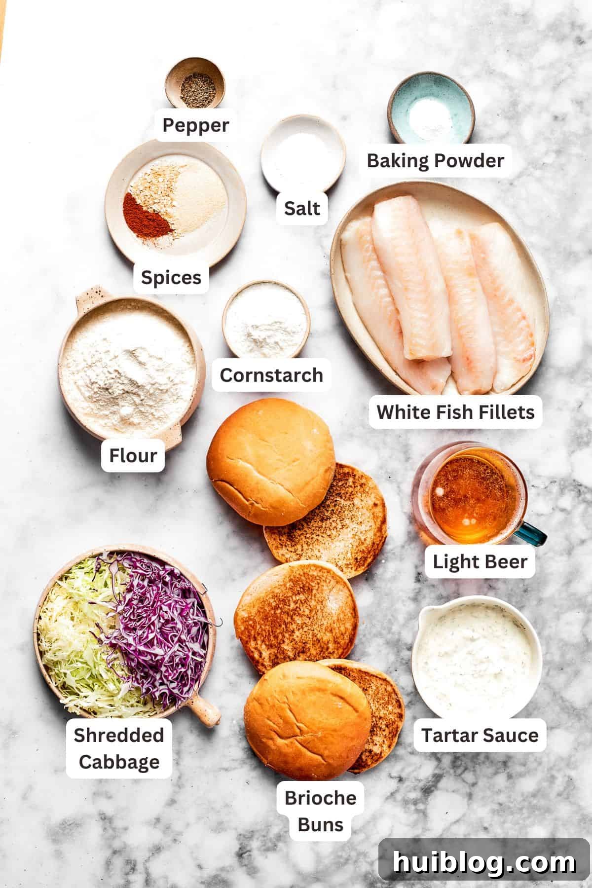This crispy, crunchy fish sandwich is served on toasty sweet rolls with lemony tartar sauce and a squeeze of lime! It's quick and easy to make! All the fresh ingredients for a homemade crispy fish sandwich are neatly laid out and text-labeled, including fish fillets, flour, beer, and fresh vegetables.