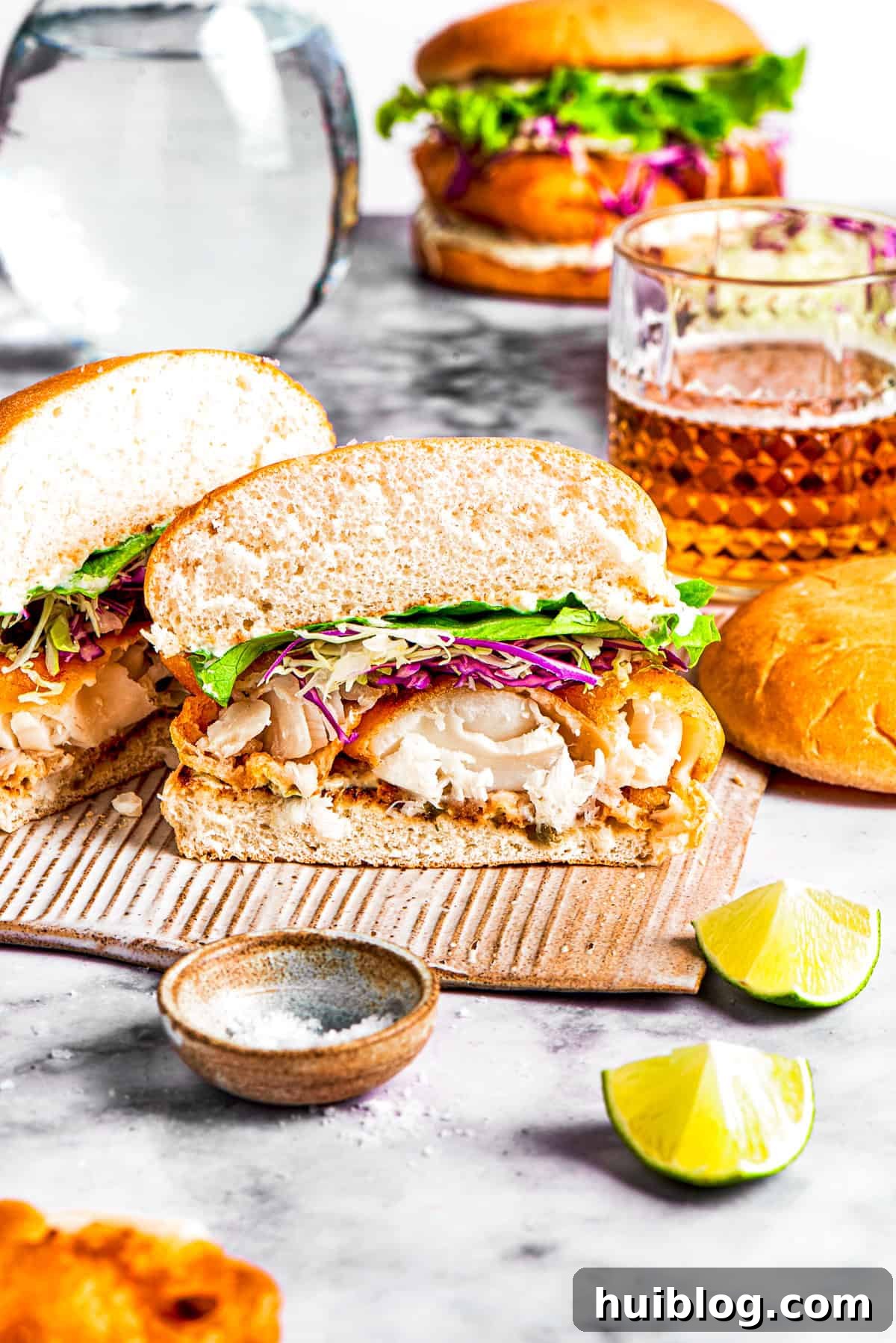 This crispy, crunchy fish sandwich is served on toasty sweet rolls with lemony tartar sauce and a squeeze of lime! It's quick and easy to make! A crispy fish sandwich, artfully cut in half, reveals the succulent fish fillet, crisp lettuce, and shredded cabbage inside a toasted bun.