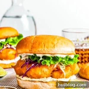 Flaky Fishwich 2 A fish sandwich on toasted buns with another sandwich and drinks placed behind it.
