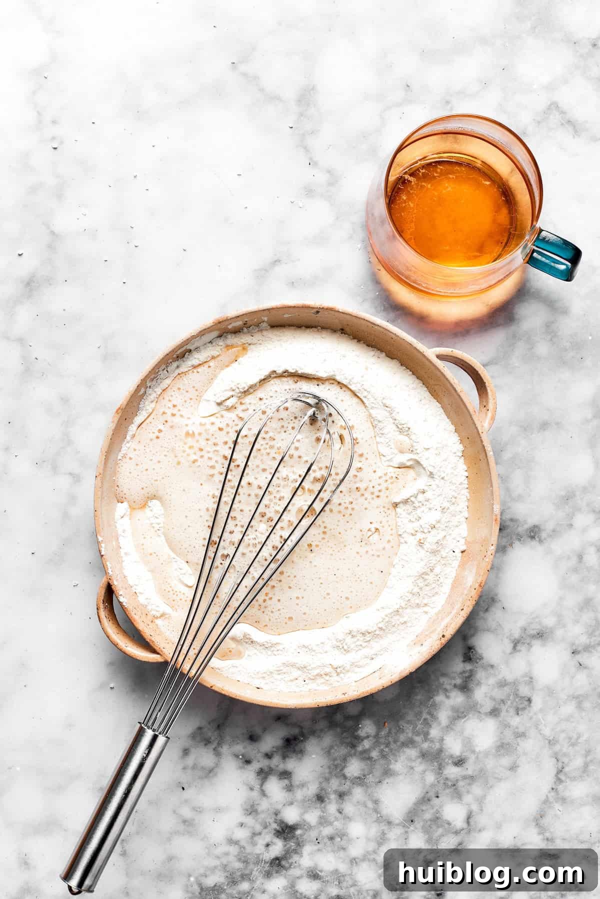 This crispy, crunchy fish sandwich is served on toasty sweet rolls with lemony tartar sauce and a squeeze of lime! It's quick and easy to make! A whisk is actively stirring a smooth, golden beer batter mixture in a mixing bowl, showcasing the ideal consistency for coating the fish.