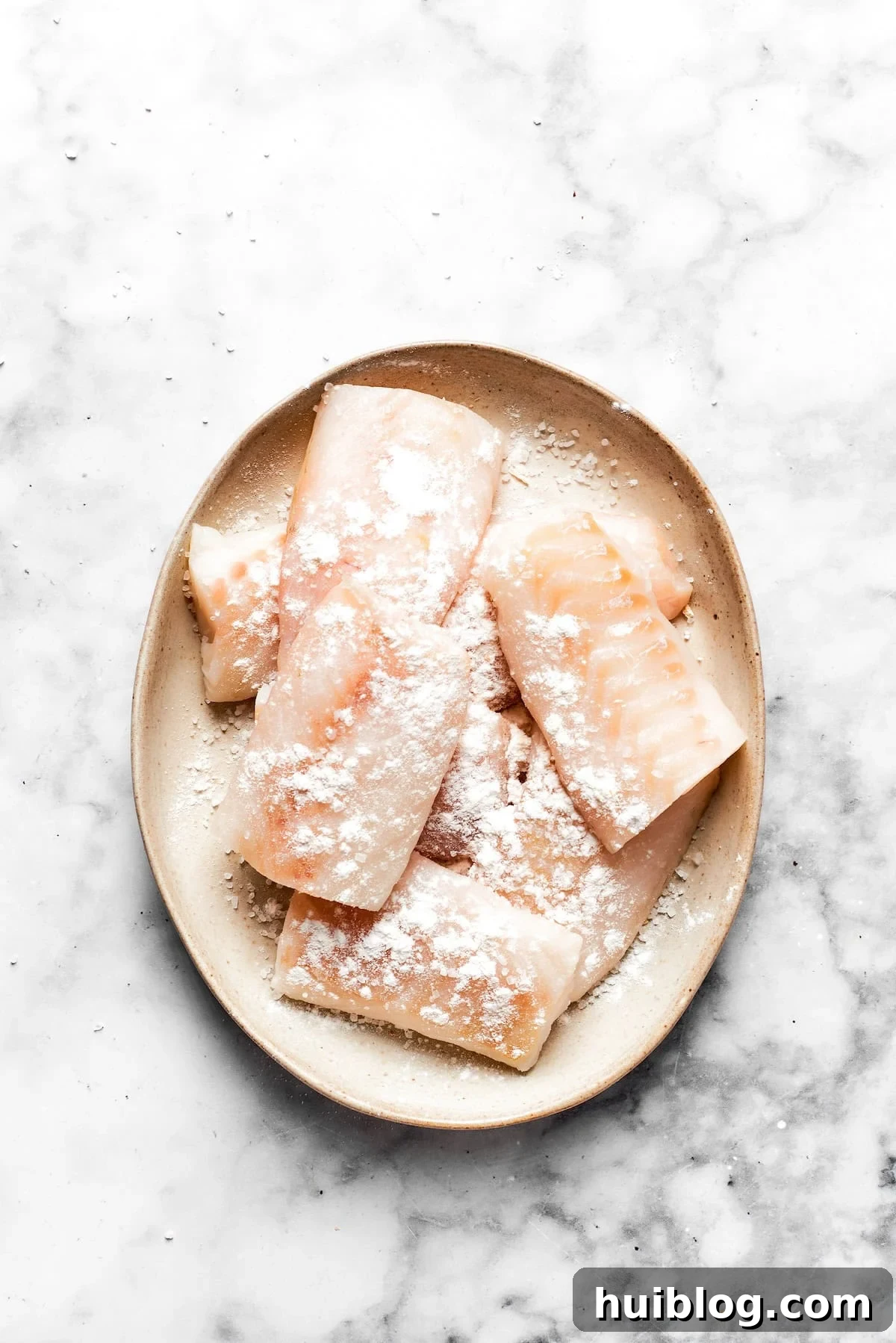This crispy, crunchy fish sandwich is served on toasty sweet rolls with lemony tartar sauce and a squeeze of lime! It's quick and easy to make! Individual fish fillets are dredged in a shallow dish of flour, showing a light and even coating before being dipped into the batter.