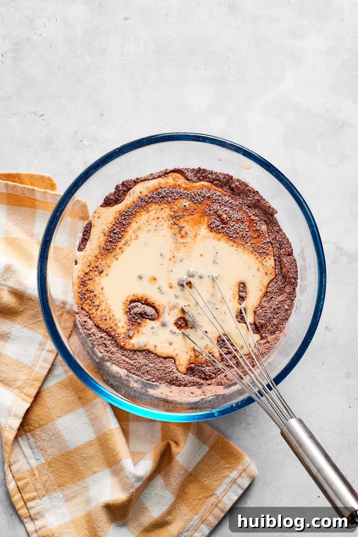 Dry and wet ingredients for chocolate muffins are gently combined in a bowl.